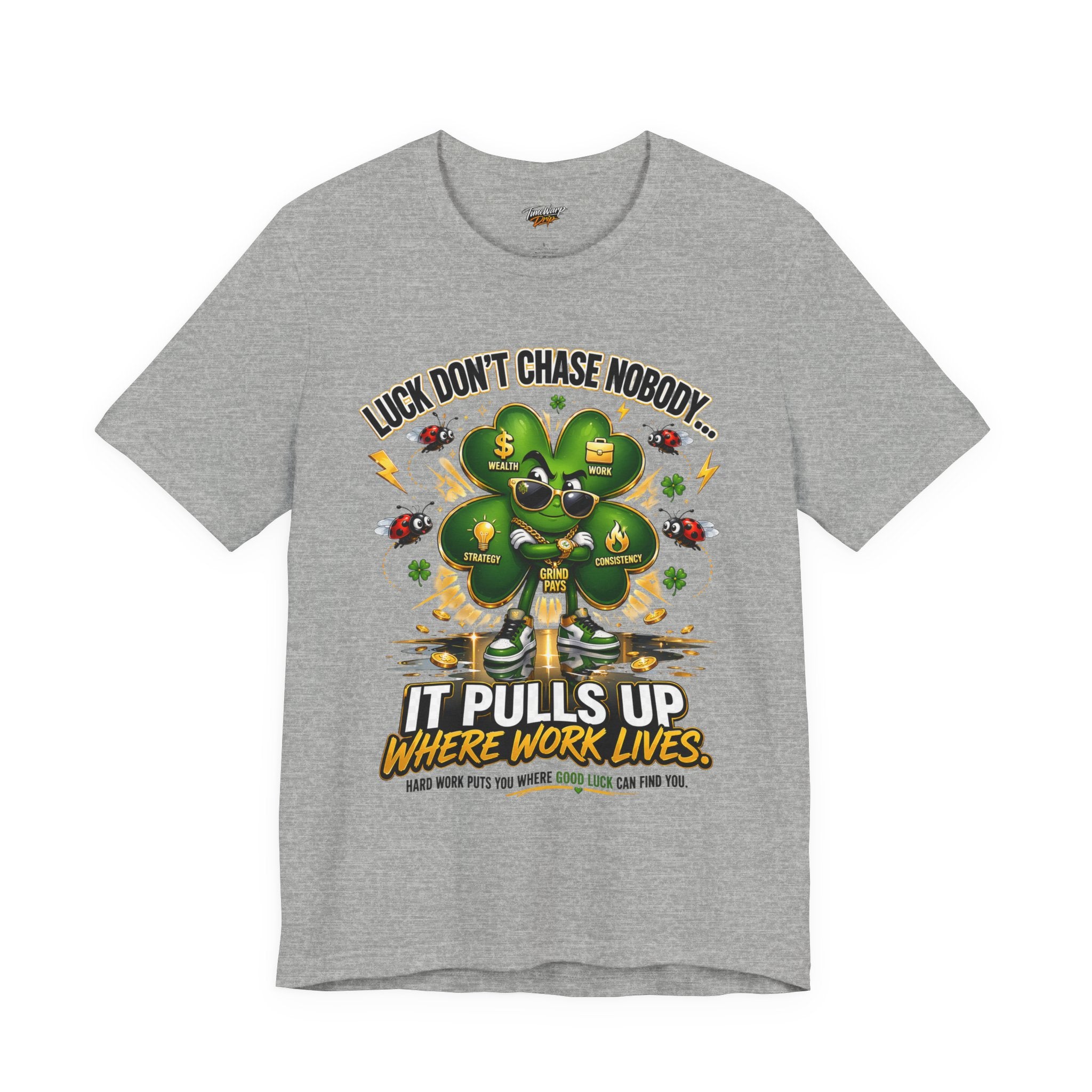 The Lucky Clover "Pulls Up Lives" Graphic T-Shirt in gray (S-3XL) features a four-leaf clover with sunglasses, coins, and ladybugs alongside the quote: Luck don’t chase nobody… it pulls up where work lives. Hard work puts you where luck finds you.