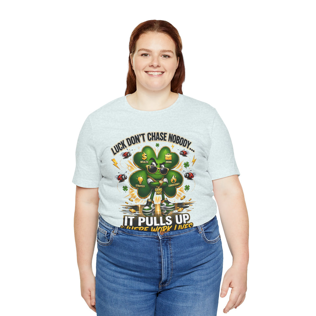 A smiling woman with long brown hair wears the TimeWarp Drip Lucky Clover "Pulls Up Lives" Graphic T-Shirt, available in S–3XL. It features a four-leaf clover, small icons, and the phrase: “Luck don’t chase nobody. It pulls up where work lives.”.