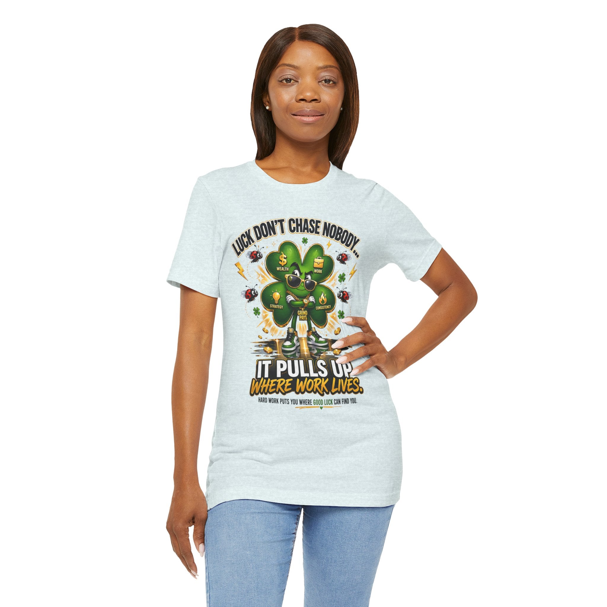 A woman with straight brown hair smiles in a TimeWarp Drip Lucky Clover "Pulls Up Lives" Graphic T-Shirt (sizes S–3XL), featuring a cartoon four-leaf clover and "Luck Don’t Chase Nobody. It Pulls Up Where Work Lives." on a plain white background.
