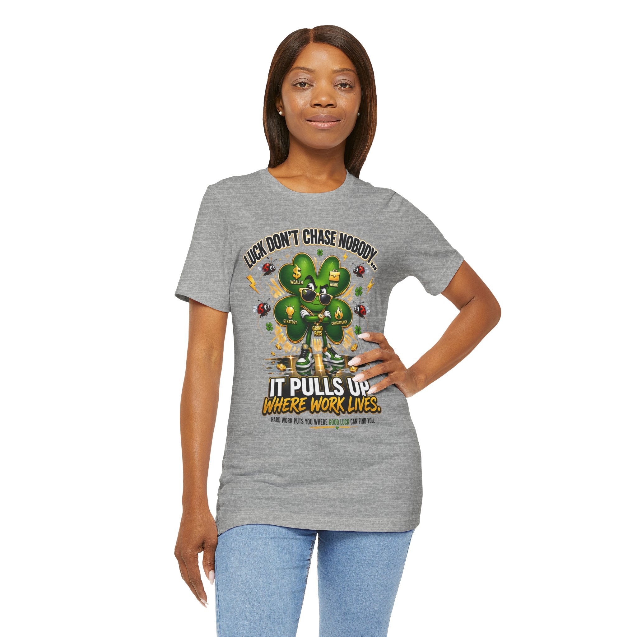 A woman models the TimeWarp Drip Lucky Clover "Pulls Up Lives" Graphic T-Shirt in gray, featuring a cartoon clover and motivational text. Available in sizes S–3XL, she stands smiling with one hand on her hip.