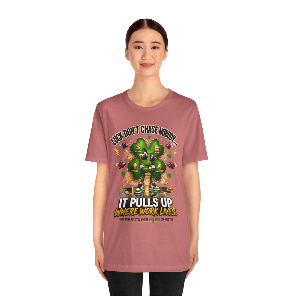 A woman wears the Lucky Clover "Pulls Up Lives" Graphic T-Shirt in pink (sizes S-3XL), featuring a cartoon clover, money, motivational phrases, and the text: Luck doesn’t chase nobody. It pulls up where work lives.