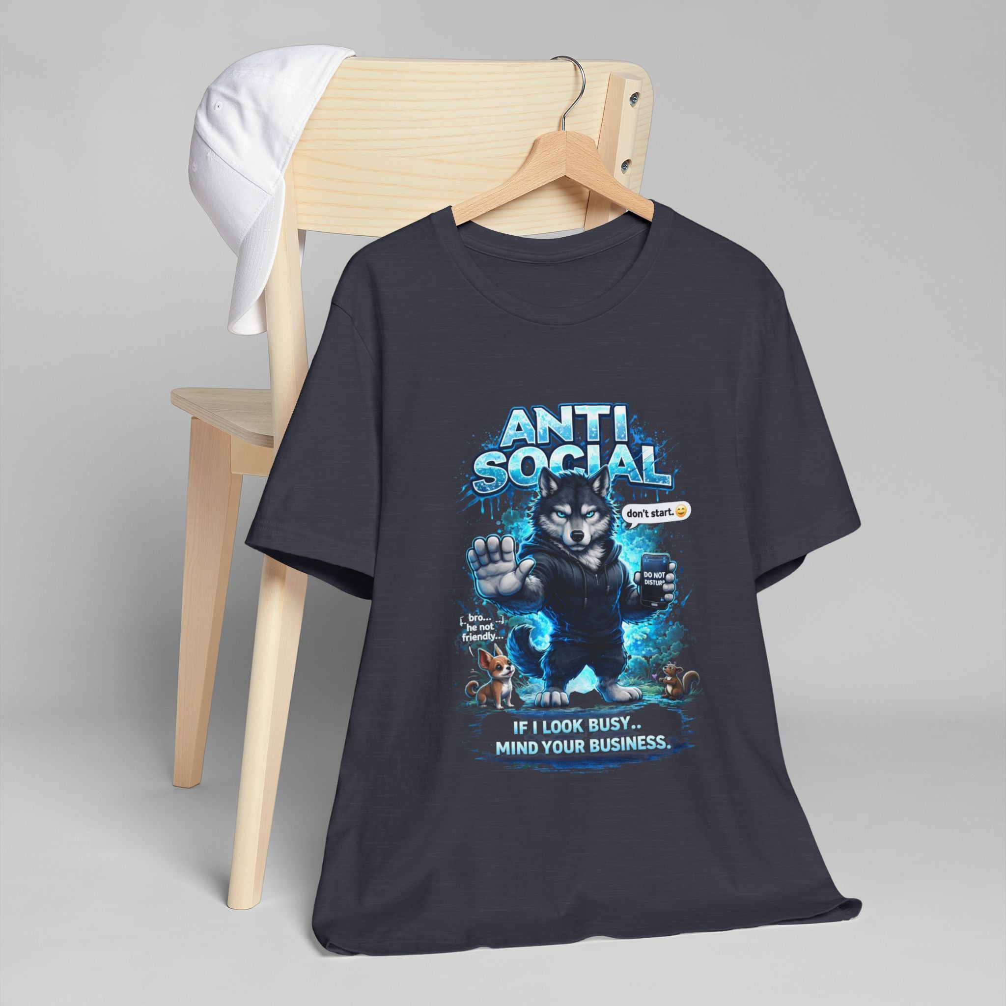 The Timewarp Drip Anti Social Wolf T-Shirt — Funny Introvert Graphic Tee is a black tee featuring a grumpy wolf with a phone and the text "ANTI SOCIAL" and "IF I LOOK BUSY... MIND YOUR BUSINESS," displayed on a wooden chair with a white cap.