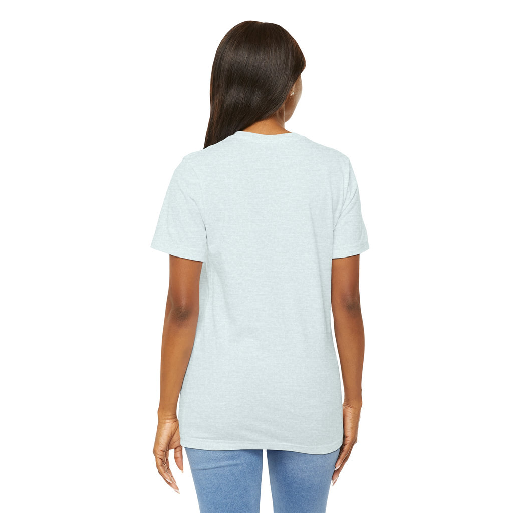 A woman with long dark hair faces away from the camera, wearing a TimeWarp Drip Lucky Clover "Pulls Up Lives" graphic t-shirt (sizes S-2XL) in light gray and light blue jeans against a plain white background.