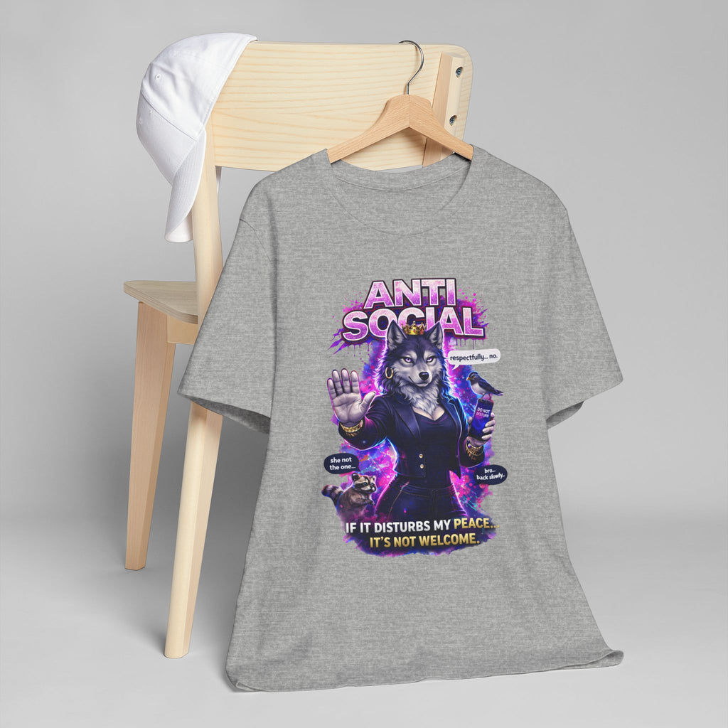 The Anti Social She-Wolf T-Shirt — a gray funny introvert graphic tee with an anthropomorphic wolf in a suit and "ANTI SOCIAL" text — hangs on a wooden chair with a white cap draped over the back, set against a plain gray background.