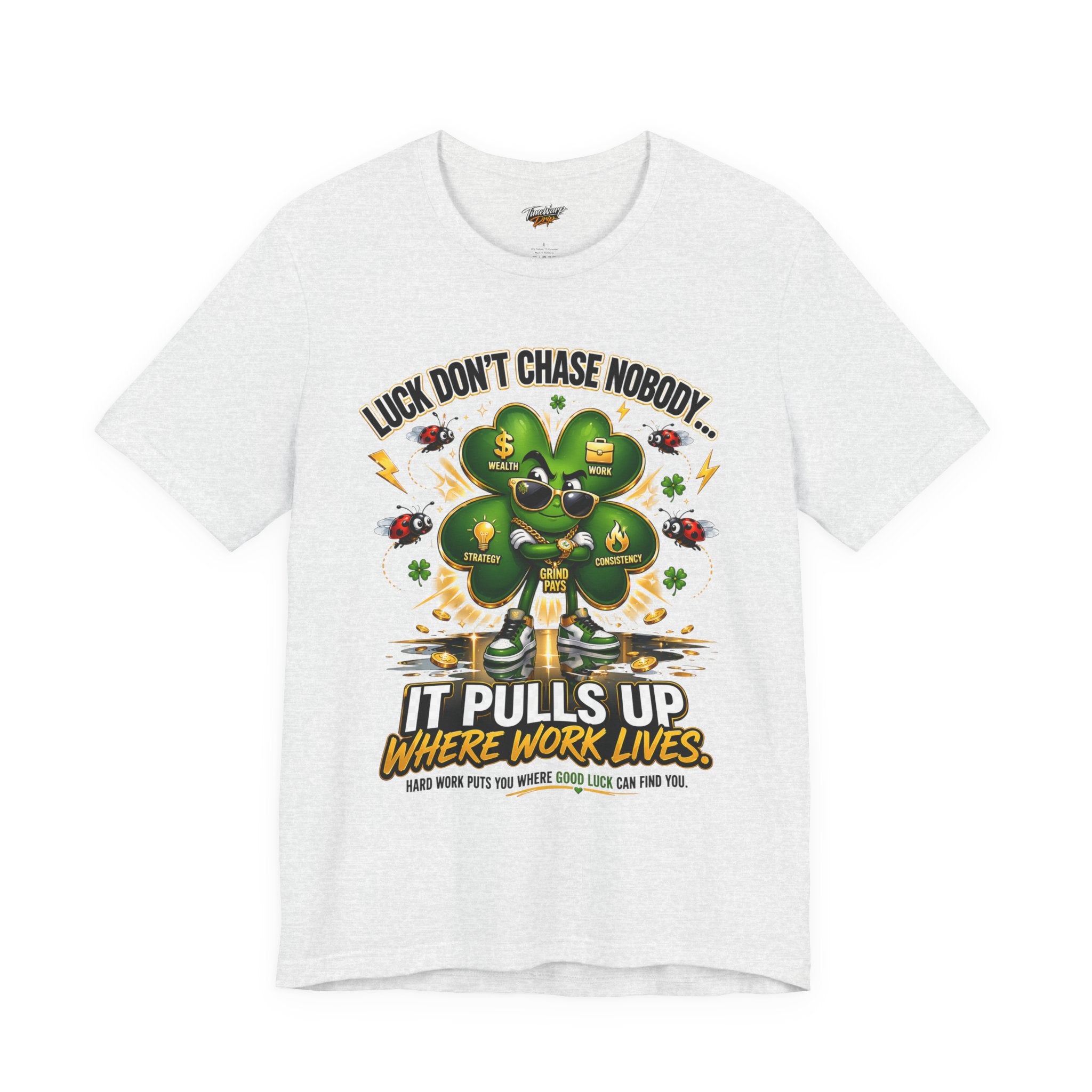 The Lucky Clover "Pulls Up Lives" Graphic T-Shirt in white, sizes S–XL and plus, shows a green four-leaf clover with sunglasses and gold shoes. Text reads: Luck Don’t Chase Nobody... It Pulls Up Where Work Lives. Hard work attracts good luck.