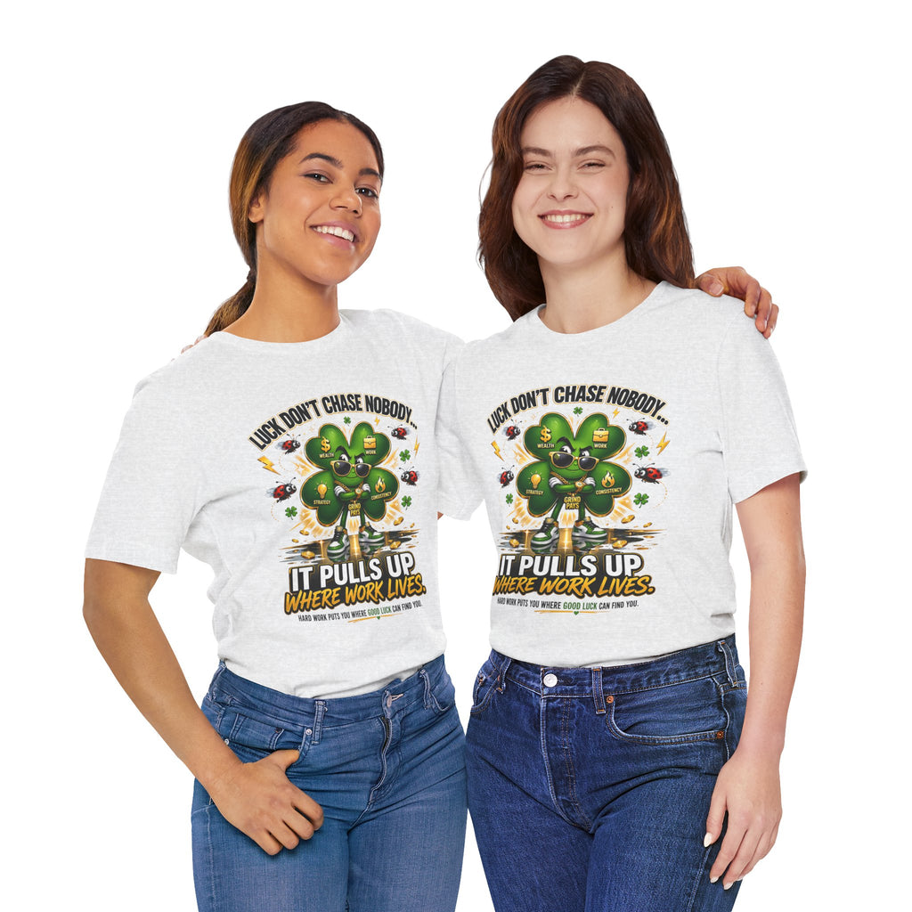 Two women smile side by side wearing TimeWarp Drip’s Lucky Clover “Pulls Up Lives” Graphic T-Shirt in sizes S–3XL, featuring a green clover and the text: Luck Don’t Chase Nobody. It Pulls Up Where Work Lives.