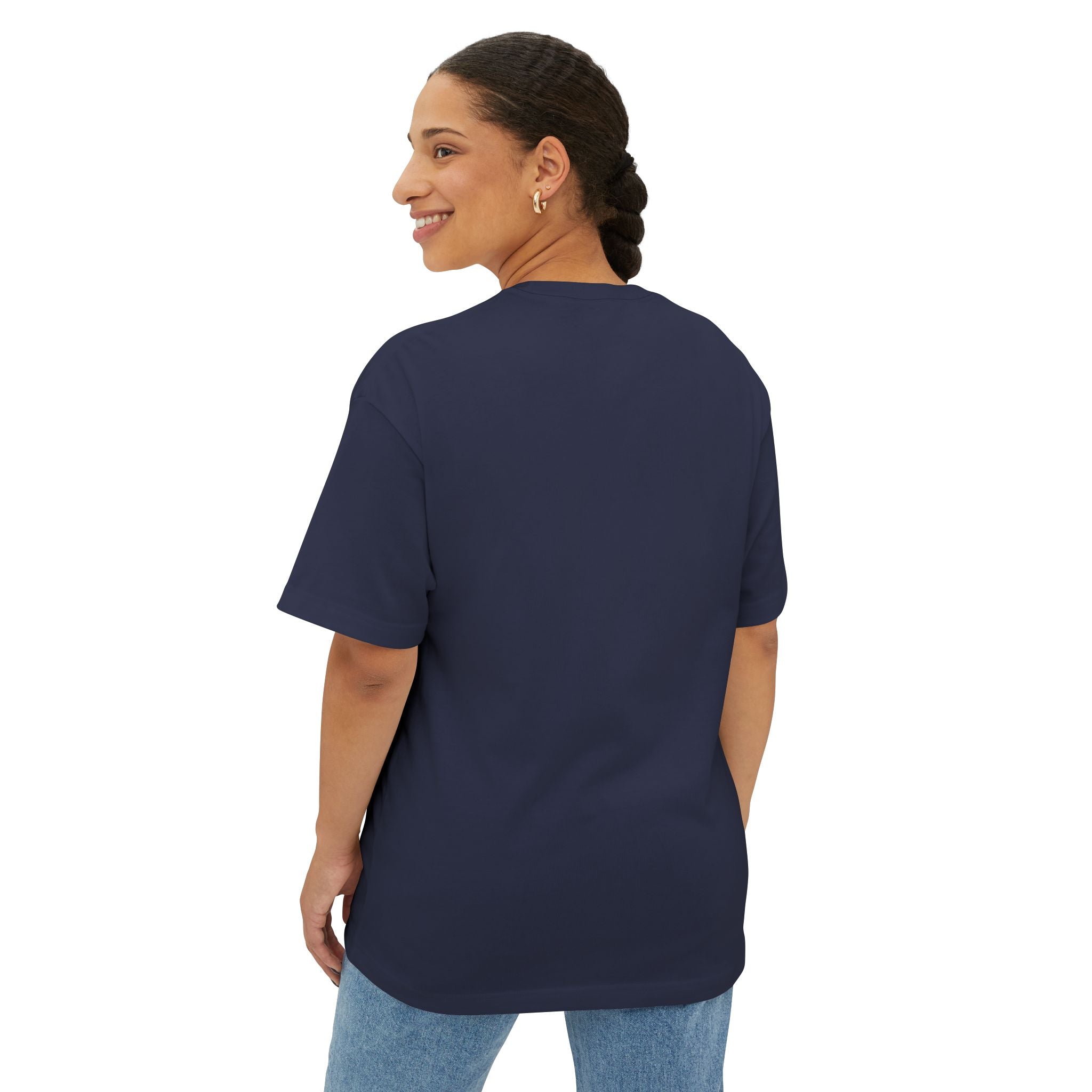 A woman with braided hair smiles over her shoulder, wearing the Crowned In Every Era Unisex Oversized Boxy Tee in navy blue and light blue jeans, standing against a plain white background.