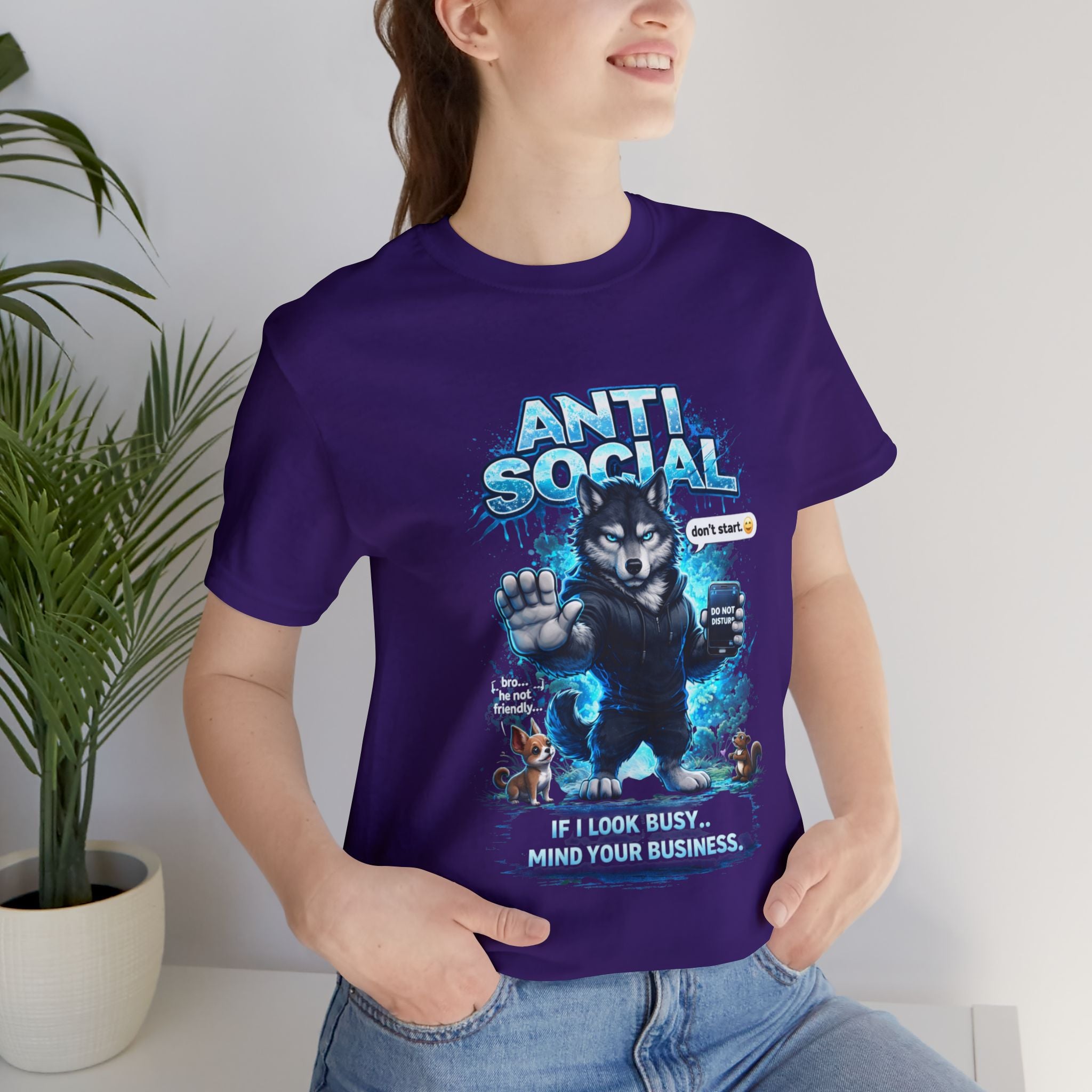 A smiling woman wears the Anti Social Wolf T-Shirt — Funny Introvert Graphic Tee by Timewarp Drip, featuring a cartoon wolf with a phone, "ANTI SOCIAL" above, "If I look busy... MIND YOUR BUSINESS," playful animals, and blue accents.