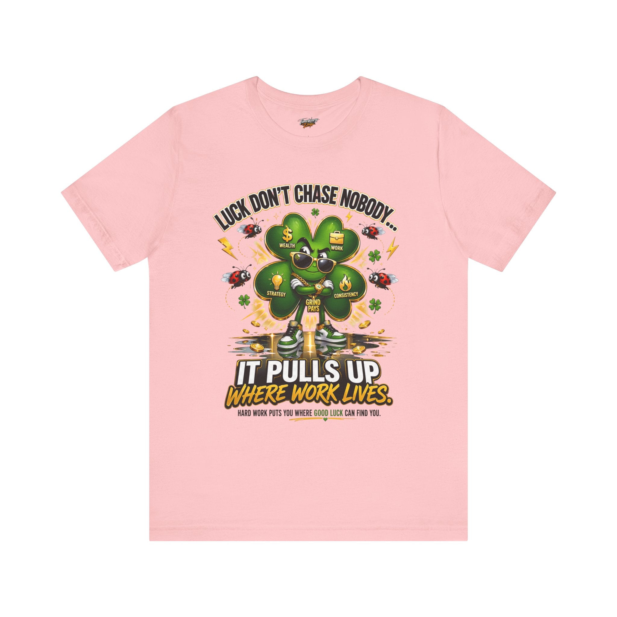 The TimeWarp Drip Lucky Clover "Pulls Up Lives" Graphic T-Shirt, in pink and sizes S–3XL, displays a bold green four-leaf clover with coins and symbols. Inspiring text and a central worker illustrate how luck and hard work combine.