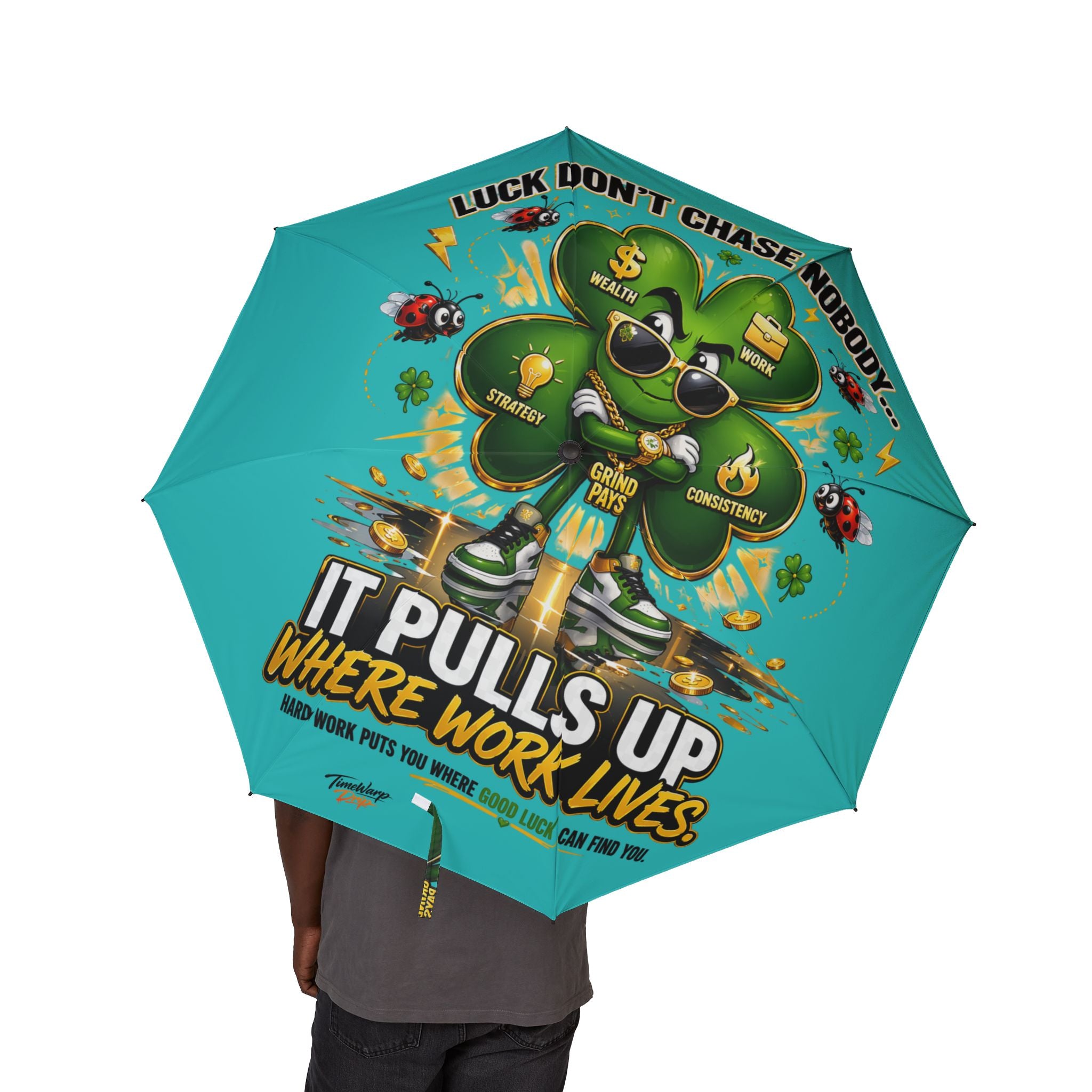 A person holds the Lucky Clover "Pulls Up Lives" foldable teal umbrella, featuring a green four-leaf clover cartoon with sunglasses and shoes, coins and lightning, plus motivational text: “Luck don’t chase nobody.”.
