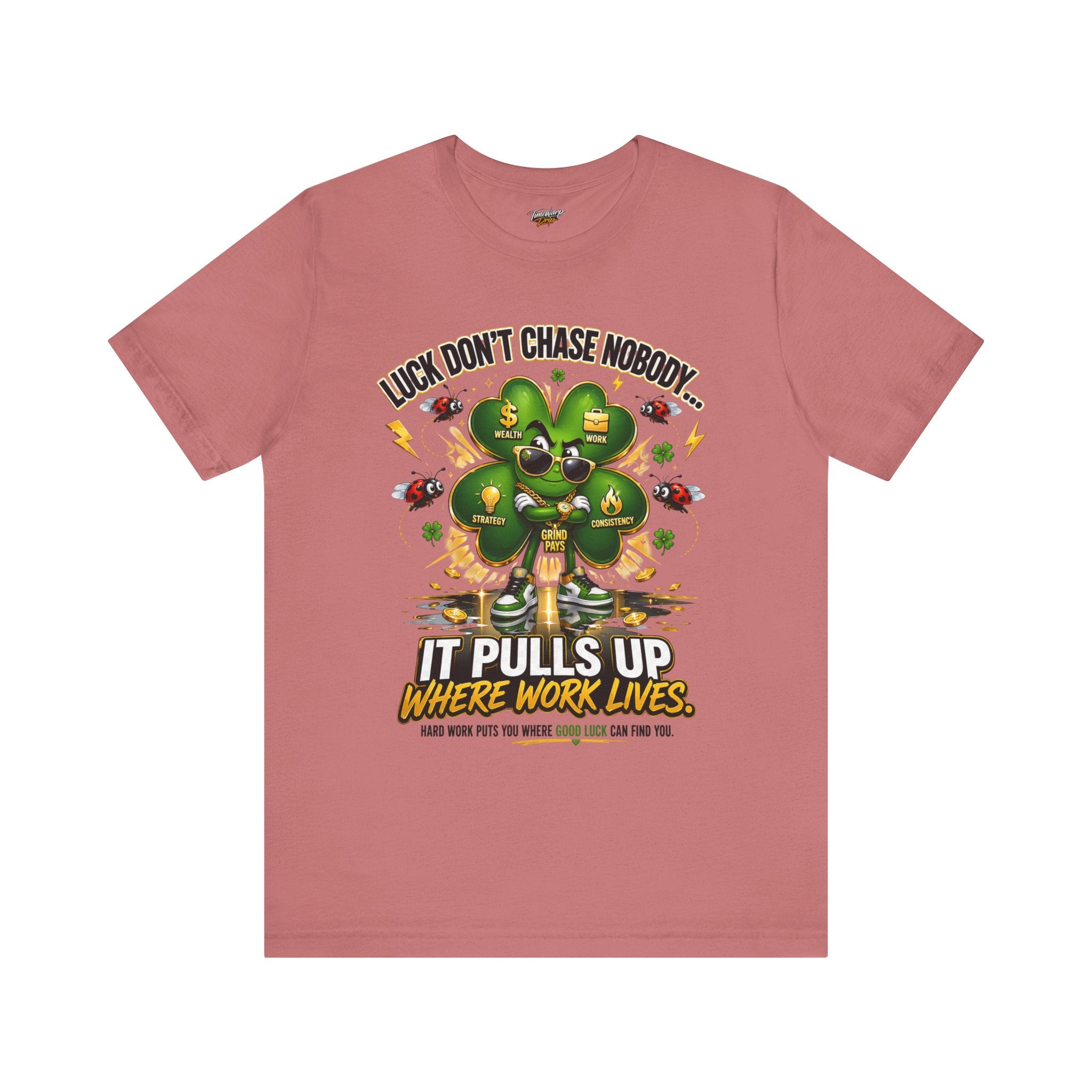 The Lucky Clover "Pulls Up Lives" Graphic T-Shirt comes in pink (S–3XL) with a clover, money bags, coins, inspiring icons, and “Luck don’t chase nobody… It pulls up where work lives” motivational text.