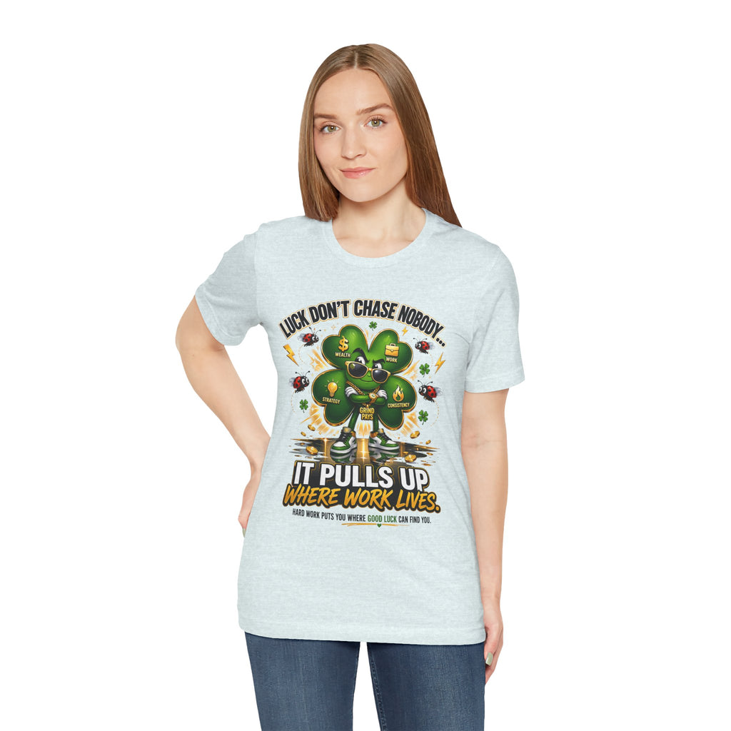 A woman with straight brown hair wears the TimeWarp Drip Lucky Clover "Pulls Up Lives" Graphic T-Shirt in light gray (sizes S-3XL), featuring a bold green shamrock with money symbols and tools, reading: Luck Don't Chase Nobody, It Pulls Up Where Work Lives.
