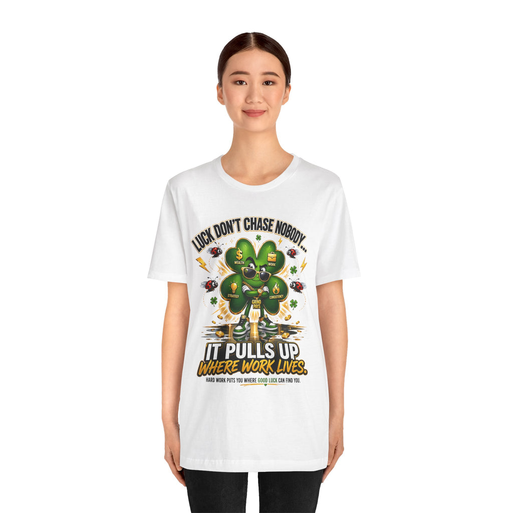 A young woman smiles in a TimeWarp Drip Lucky Clover "Pulls Up Lives" Graphic T-Shirt, featuring a colorful cartoon four-leaf clover and the phrase, "Luck, don’t chase nobody. It pulls up where work lives." Sizes: S–3XL.