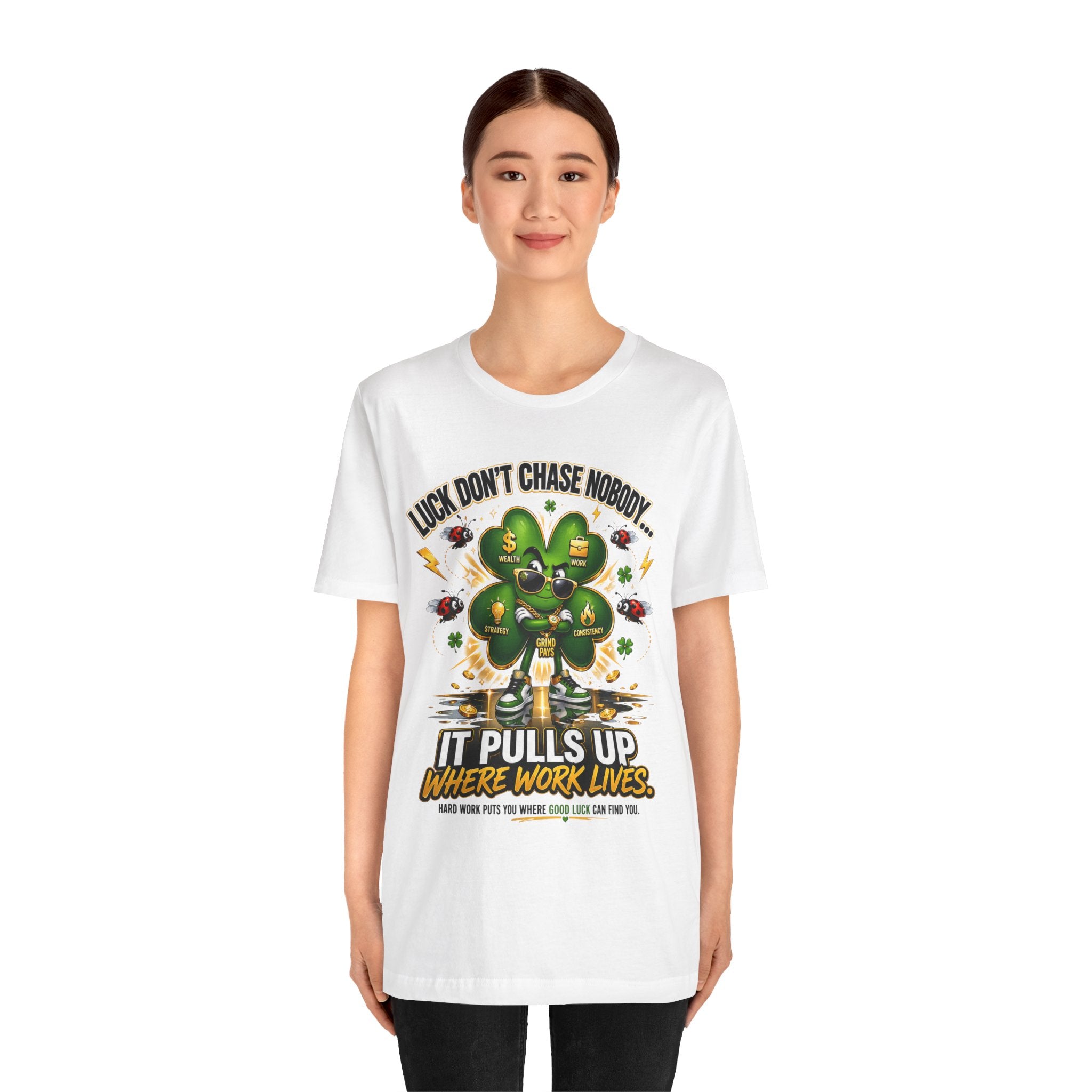 A young woman smiles in a TimeWarp Drip Lucky Clover "Pulls Up Lives" Graphic T-Shirt, featuring a colorful cartoon four-leaf clover and the phrase, "Luck, don’t chase nobody. It pulls up where work lives." Sizes: S–3XL.