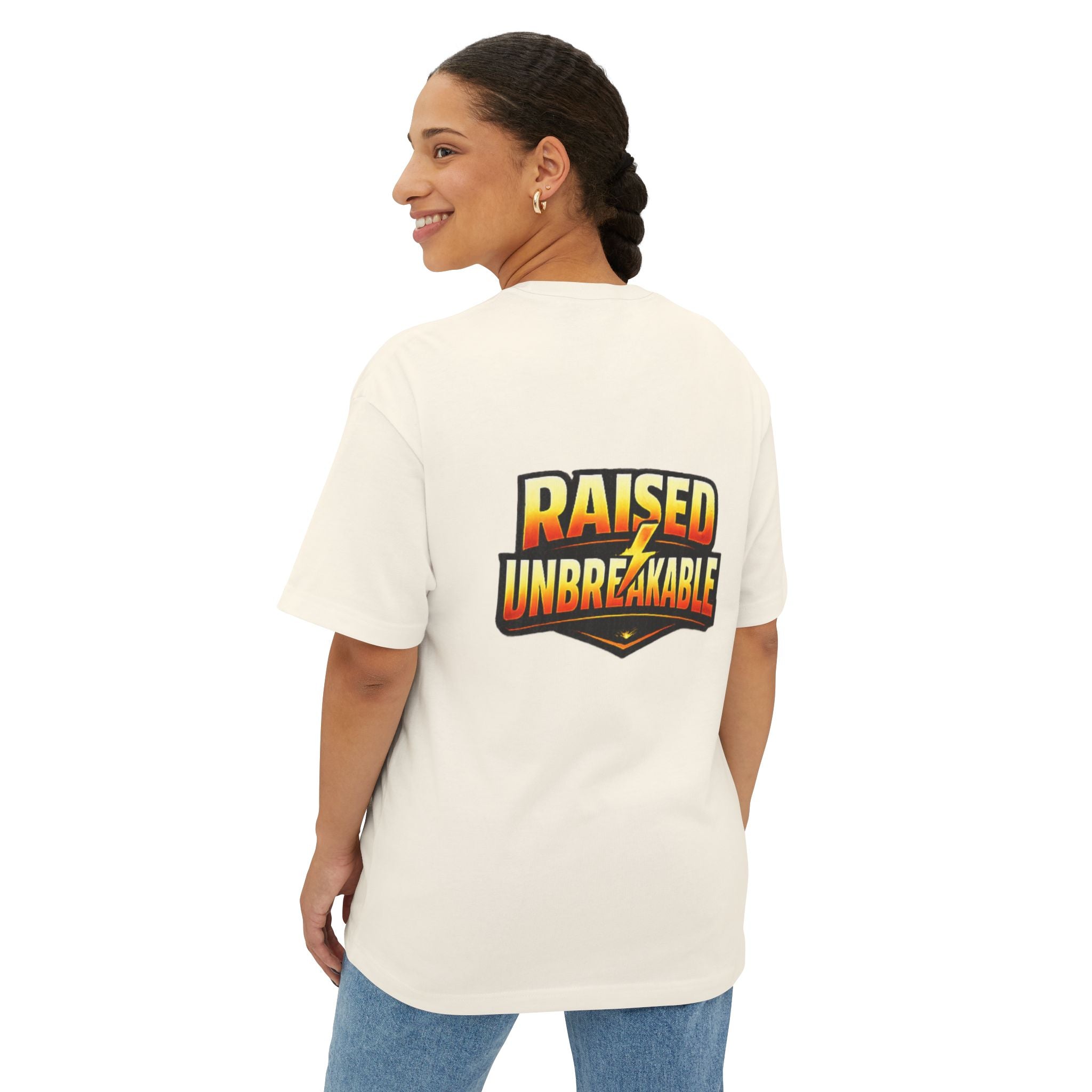 A woman with braided hair smiles over her shoulder in the Generation X Parenting "Come Get Em" oversized boxy tee by TimeWarp Drip, featuring “RAISED UNBREAKABLE” in bold, colorful letters on the back. She pairs it with blue jeans.
