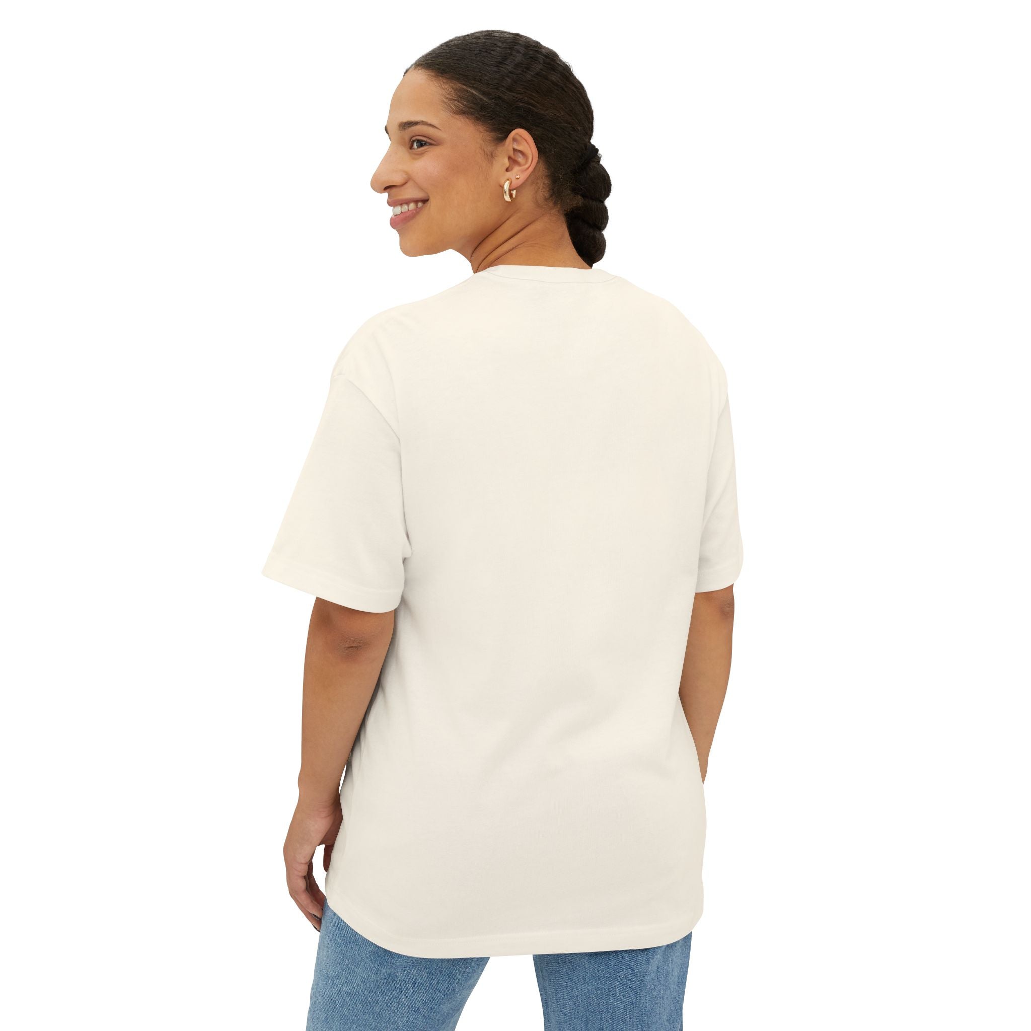 A person with braided hair, wearing the Crowned In Every Era - Unisex Oversized Boxy Tee and blue jeans, stands facing away and looks over their shoulder, smiling against a white background.