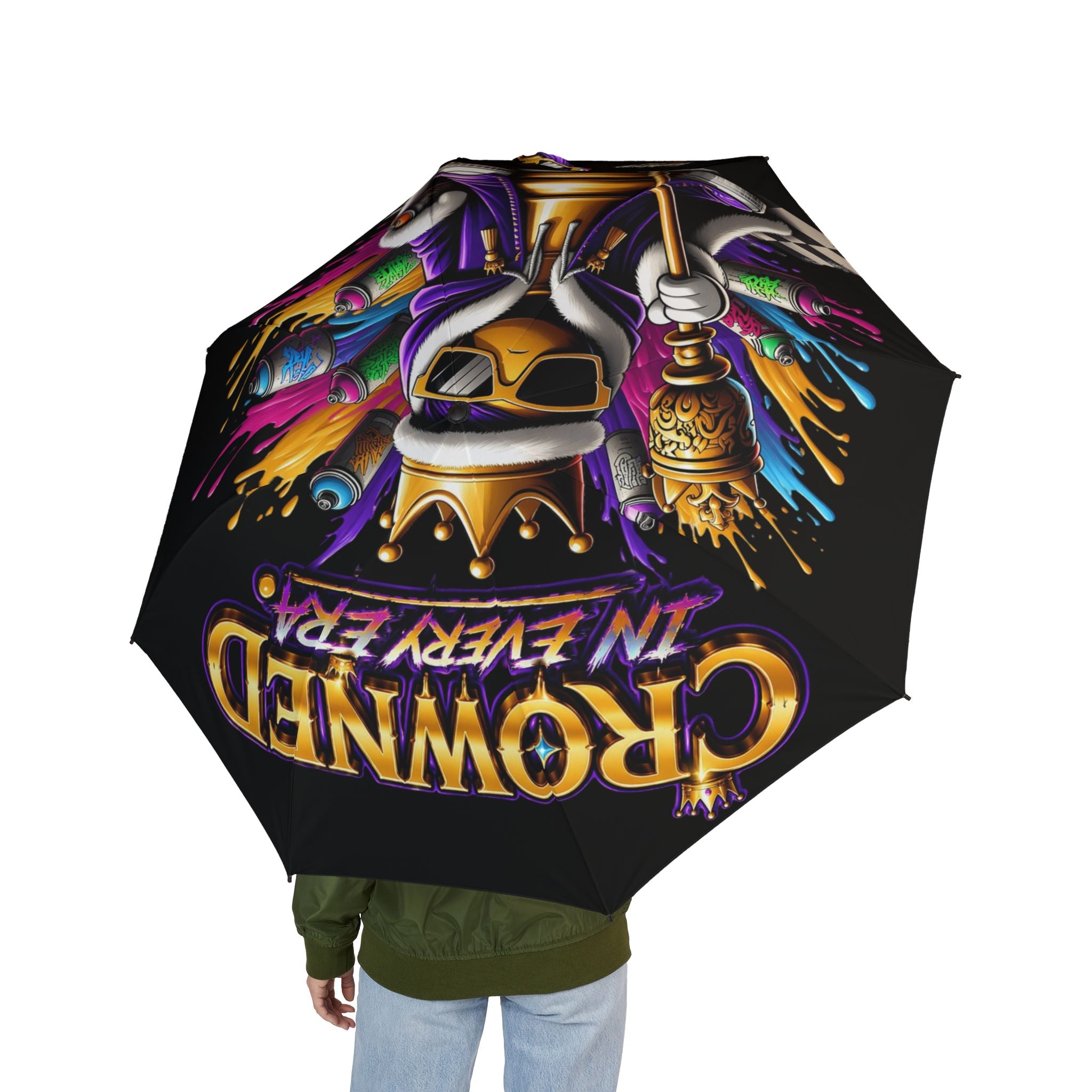 A person holds the Bold "Crowned In Every Era" Design (Black) Semi-Automatic Umbrella, featuring vibrant graffiti art of a crowned figure and gold lettering.