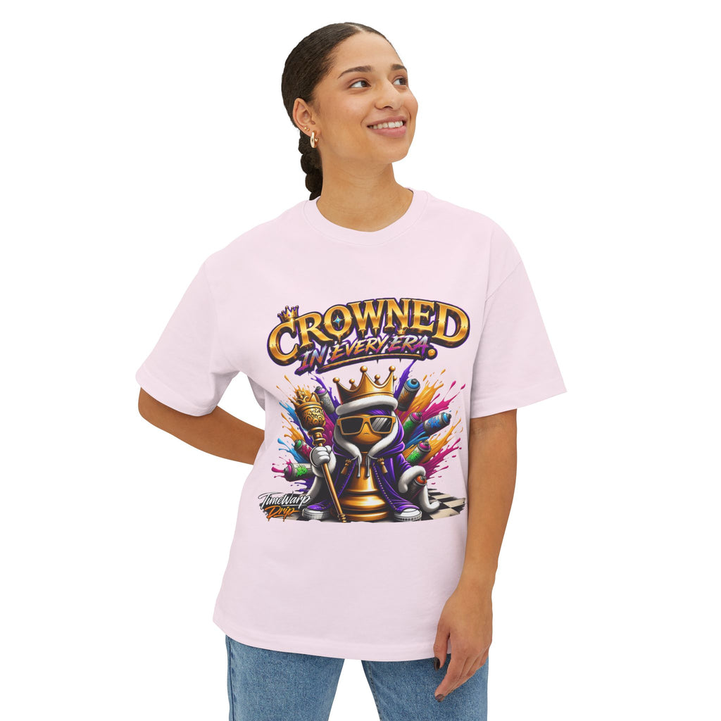 A smiling person with braided hair wears the Crowned In Every Era Unisex Oversized Boxy Tee, a light pink relaxed fit shirt featuring a colorful graphic of a crowned cartoon character with sunglasses and playful text.