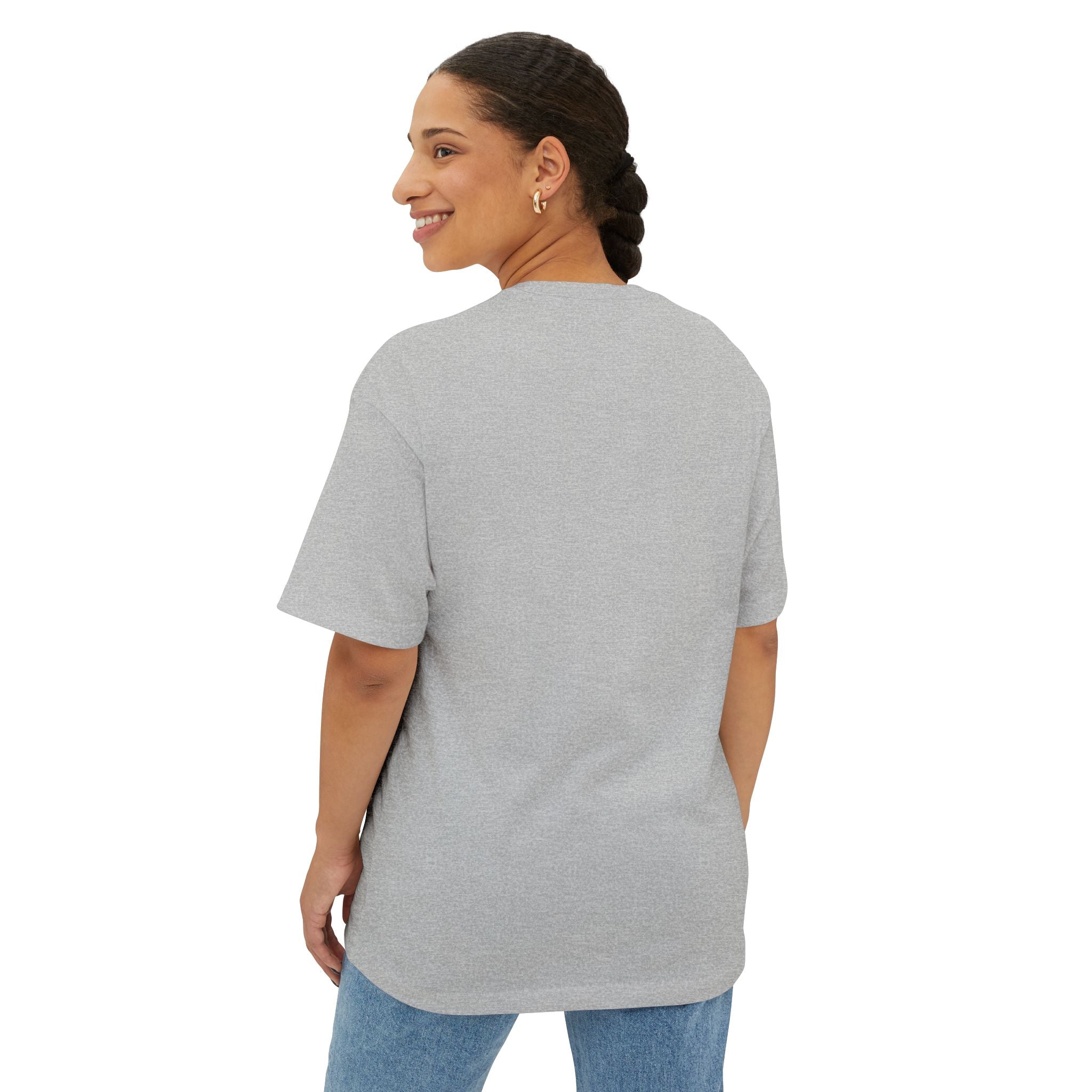 A woman with braided hair smiles over her shoulder, modeling the Crowned In Every Era Unisex Oversized Boxy Tee in light gray and blue jeans against a plain white background.