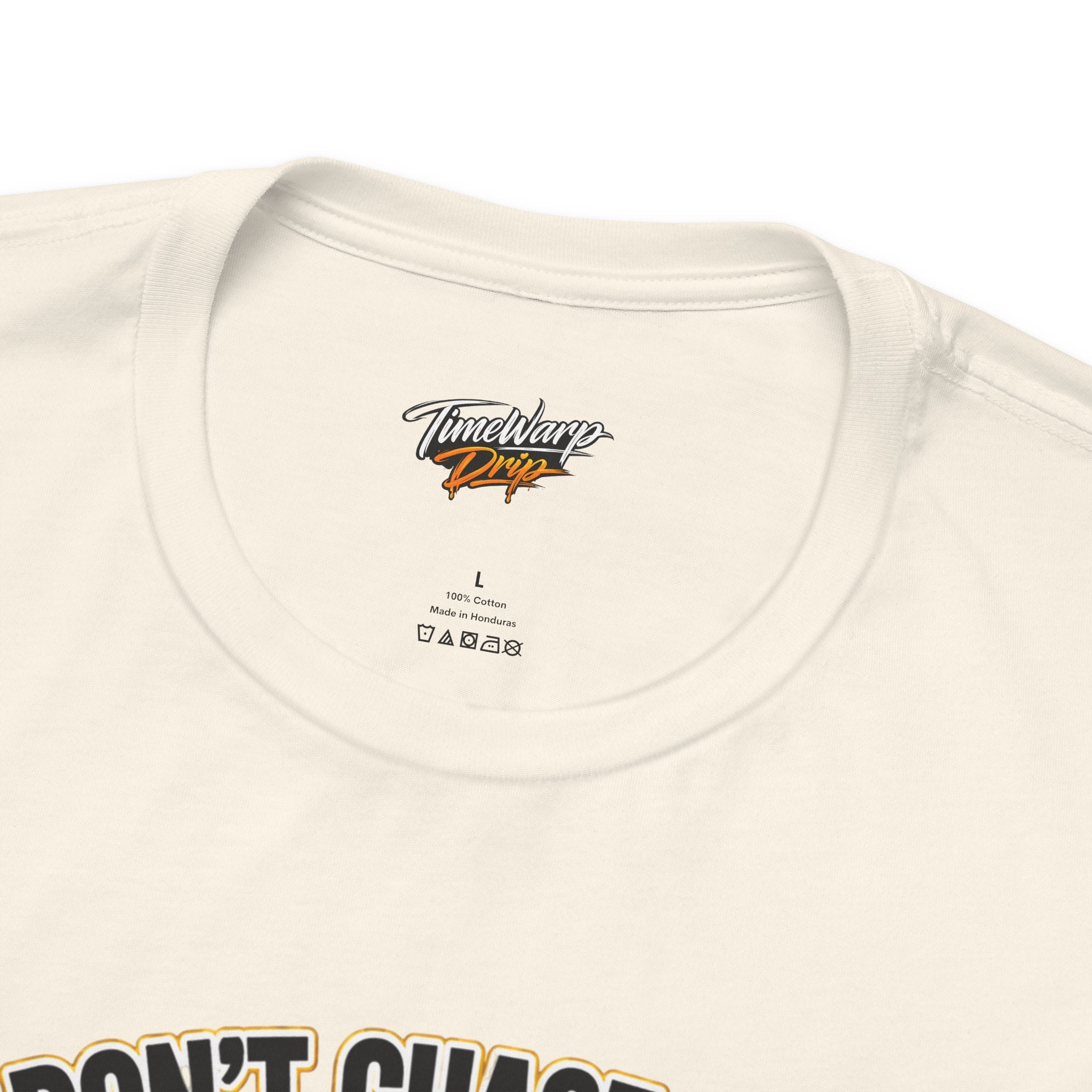A close-up of a white Lucky Clover "Pulls Up Lives" Graphic T-Shirt collar, showing S M L XL 2XL 3XL size label, branding, care instructions, and part of the bold front graphic.