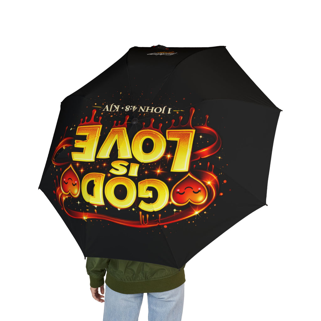 A person holds the "God Is Love" Design (Semi‑Automatic) Foldable Black Umbrella, featuring bold yellow and red “GOD IS LOVE” text, heart shapes, “1 JOHN 4:8 KJV,” and a wide one-size canopy; their face is hidden.