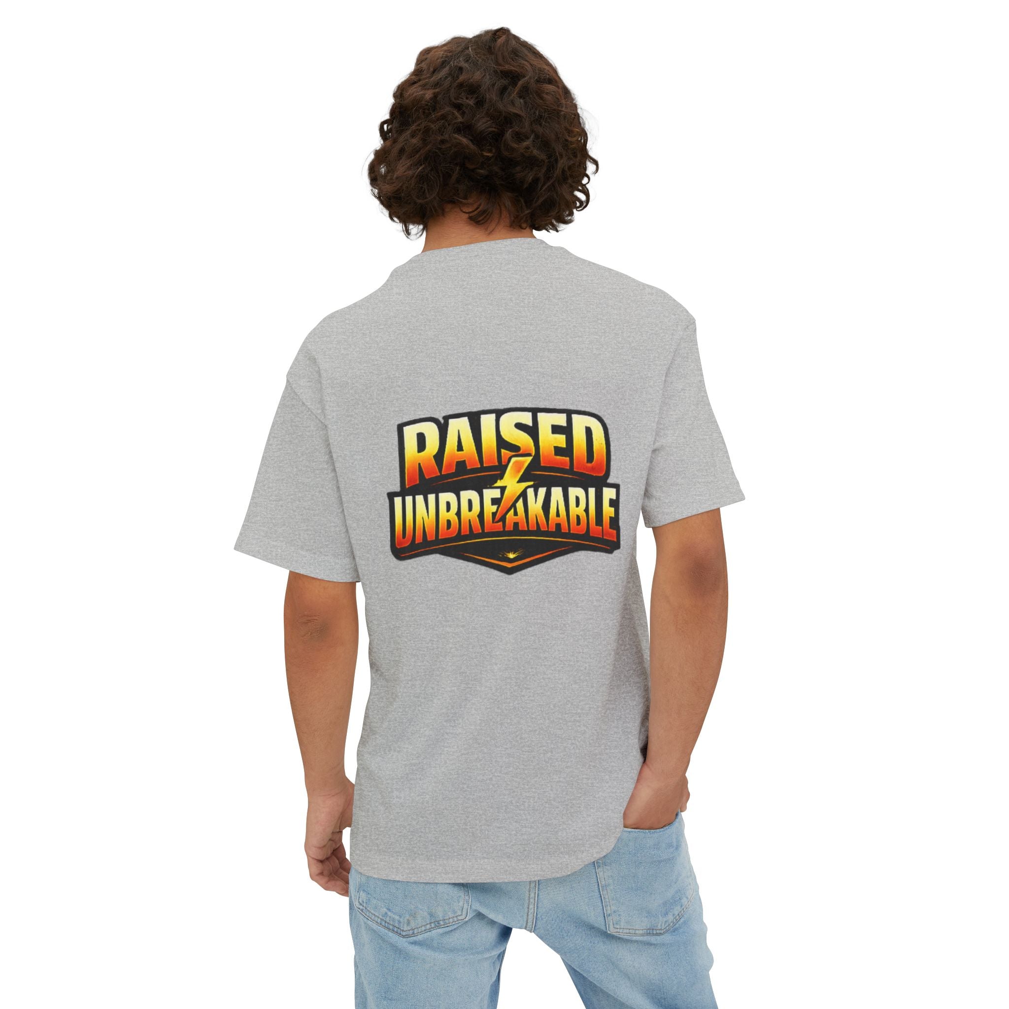 A person with curly hair, seen from behind, wears the TimeWarp Drip Generation X Parenting "Come Get Em" oversized boxy t-shirt in gray cotton, featuring bold yellow and orange "RAISED UNBREAKABLE" text on the back. One hand is casually placed in their pocket.