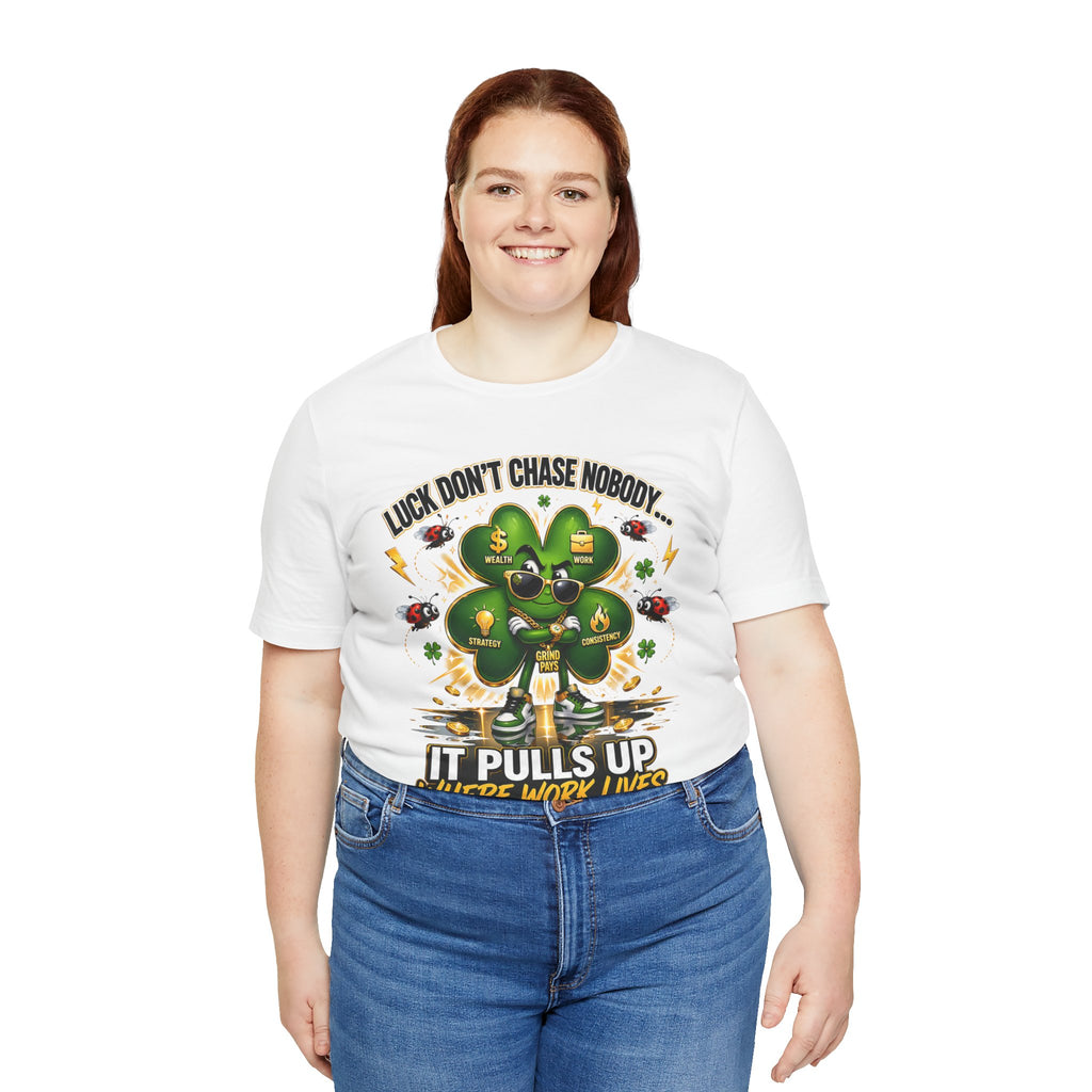 A smiling woman with long brown hair wears the TimeWarp Drip Lucky Clover "Pulls Up Lives" Graphic T-Shirt (S-3XL), featuring a shamrock and ‘Luck Don’t Chase Nobody – It Pulls Up Where Work Lives,’ against a white background.