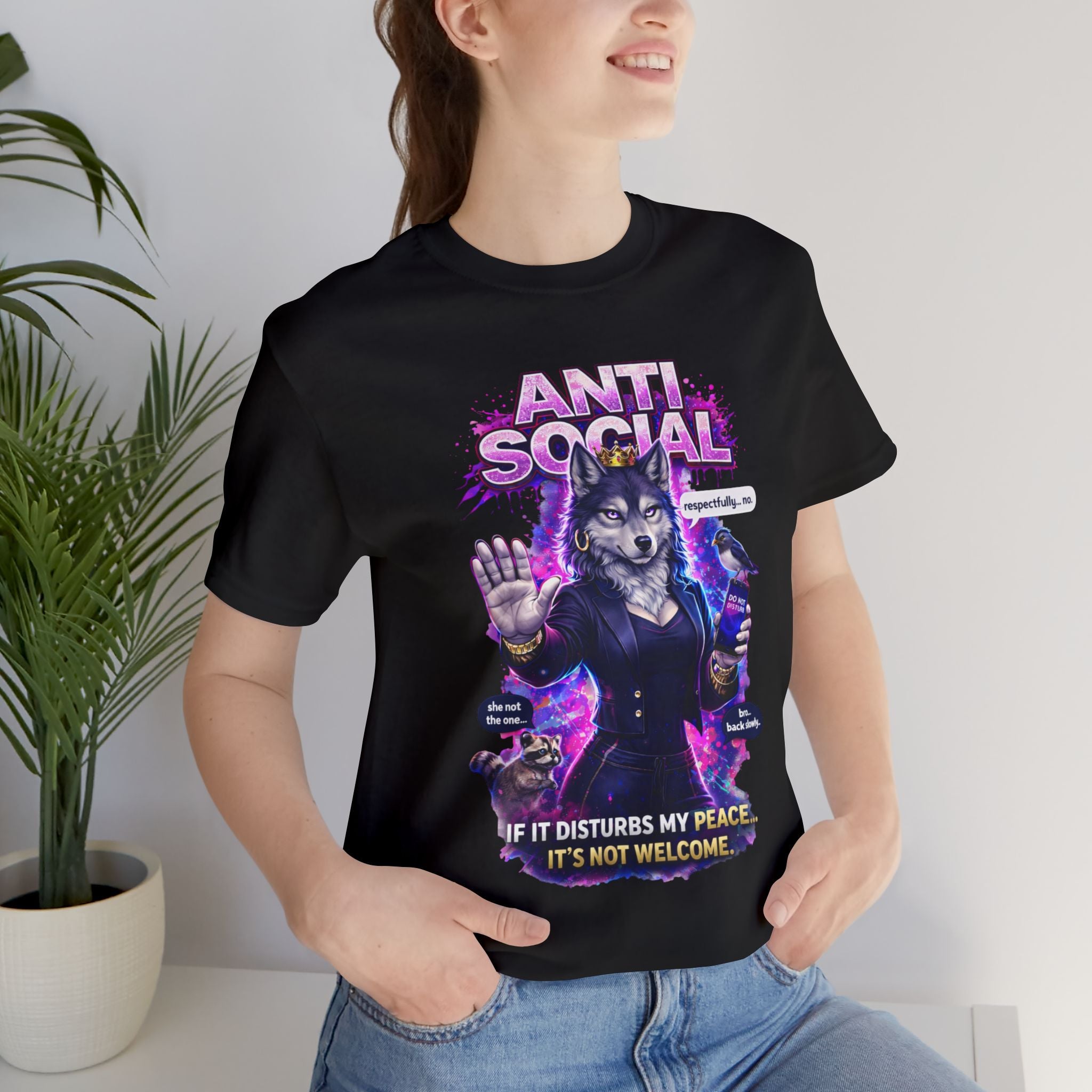 Wearing the Anti Social She-Wolf T-Shirt — a funny introvert graphic tee with an anti-social wolf in a suit and witty sayings — a person stands by a plant and smiles.
