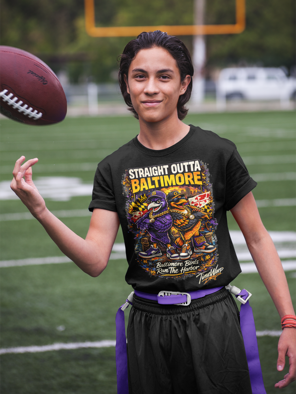 TimeWarp Drip Teen flexes in black Straight Outta Baltimore tee by TimeWarp Drip, throwing a football with bold streetwear vibes near goalposts. streetwear apparel