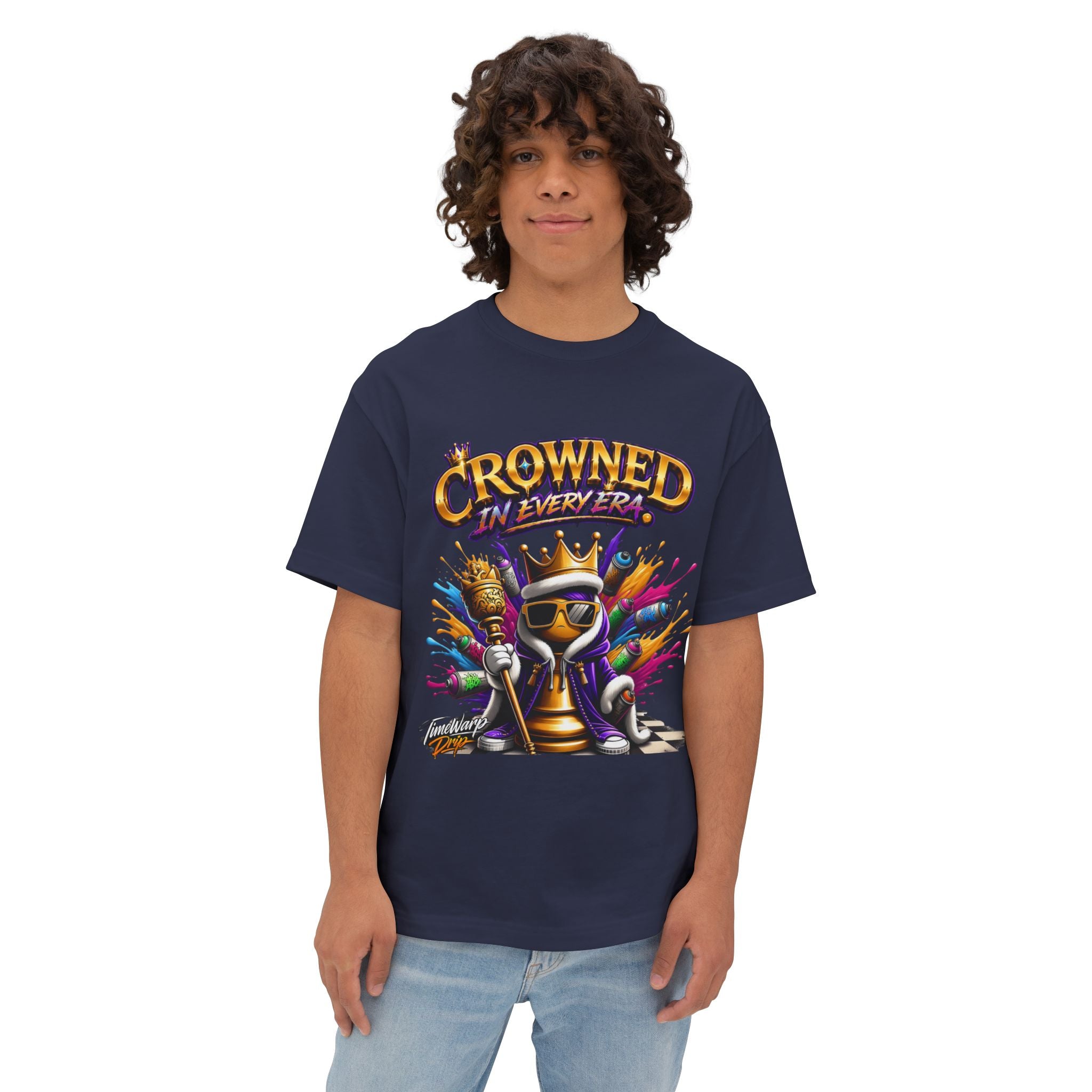 A person with curly hair wears the navy blue "Crowned In Every Era - Unisex Oversized Boxy Tee," featuring a colorful crowned chess piece and text, styled in a relaxed fit against a plain background.