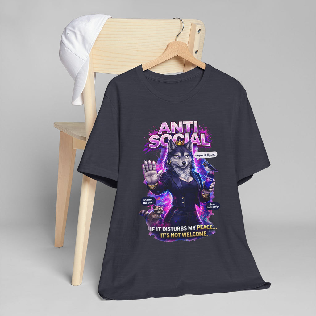 The Anti Social She-Wolf T-Shirt—Funny Introvert Graphic Tee—features a black shirt with a suited, glasses-wearing wolf holding coffee, plus the text: "ANTI SOCIAL" and "If it disturbs my peace... It's not welcome." A white cap sits nearby.