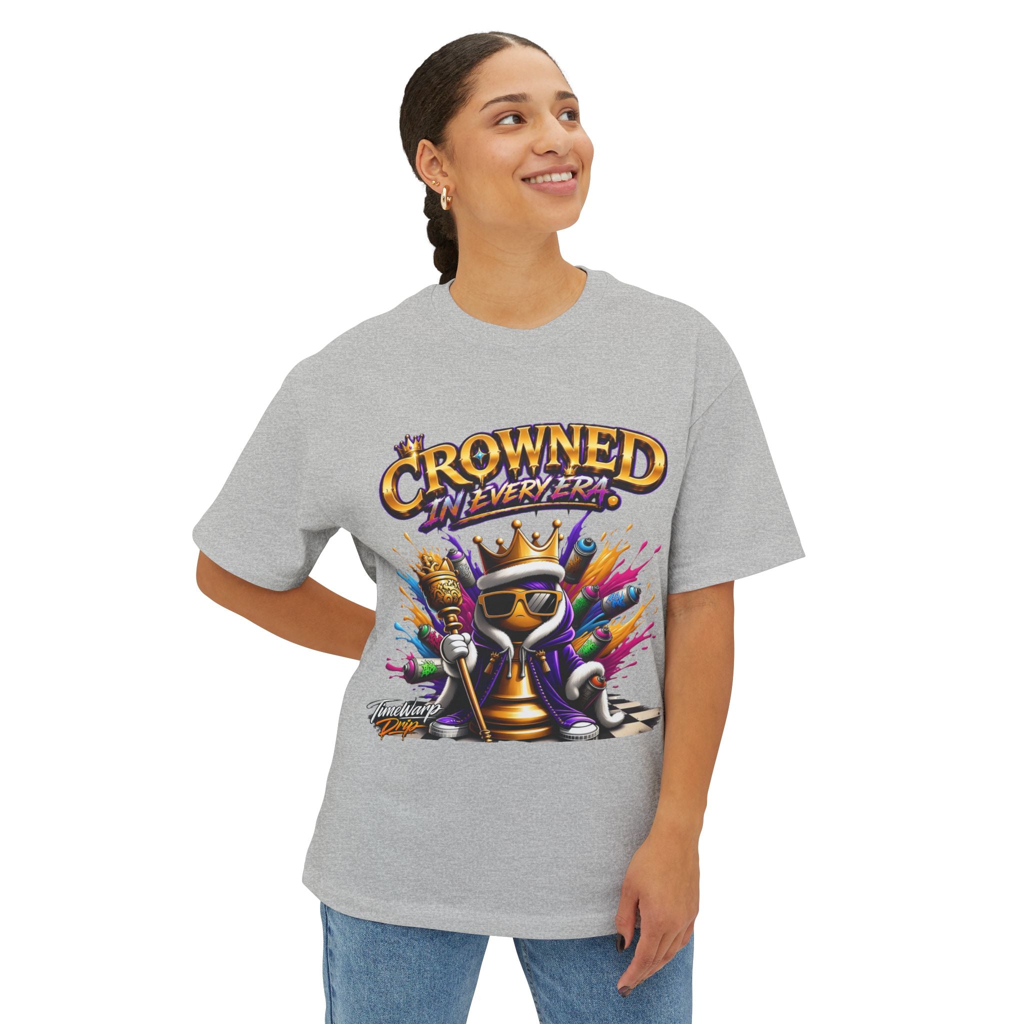 A woman smiles, wearing the "Crowned In Every Era" Unisex Oversized Boxy Tee in light gray, featuring a crowned cartoon frog in sunglasses holding money and the phrase "Crowned in Every Era" above. Made from airlume combed cotton.