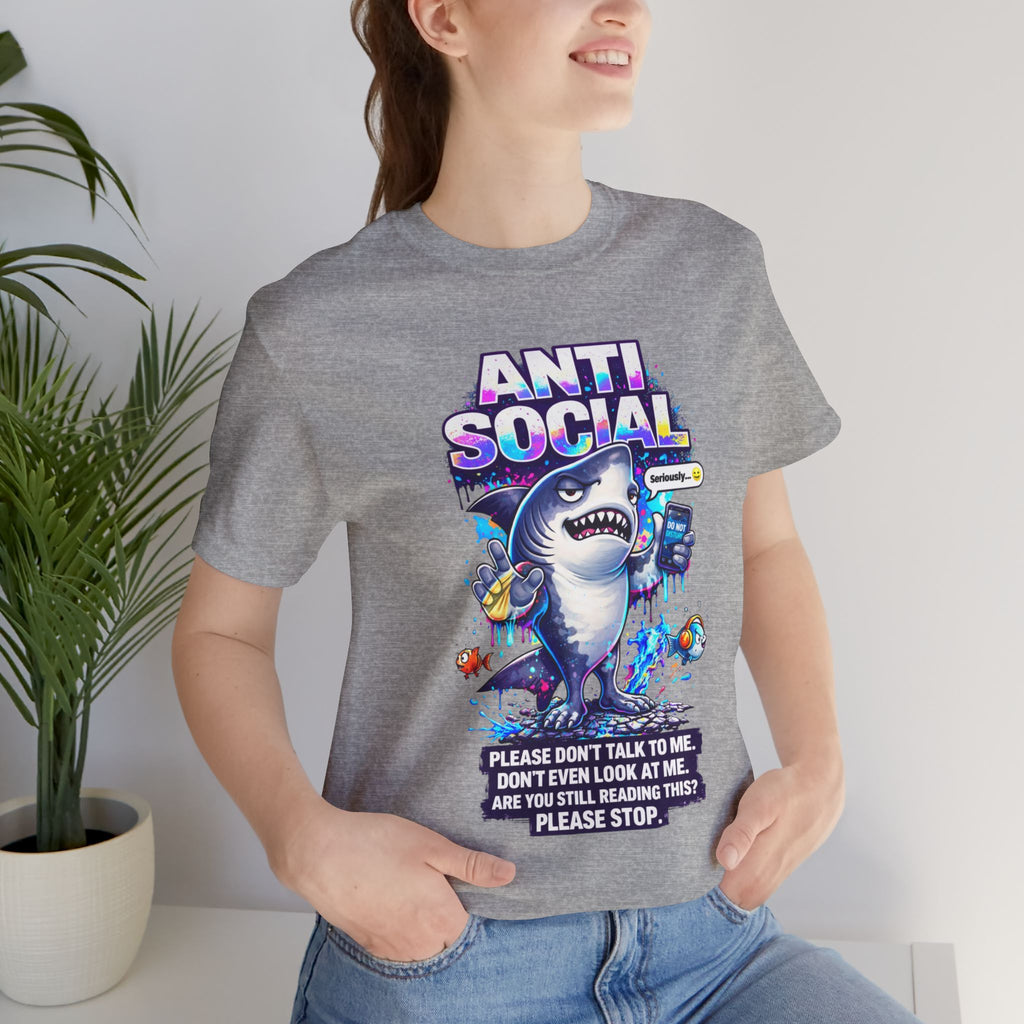 A smiling person wears the Anti Social Shark T-Shirt — Funny Introvert Graphic Tee, showing off its playful shark graphic and bold lettering indoors, with a leafy plant adding to the cozy vibe.