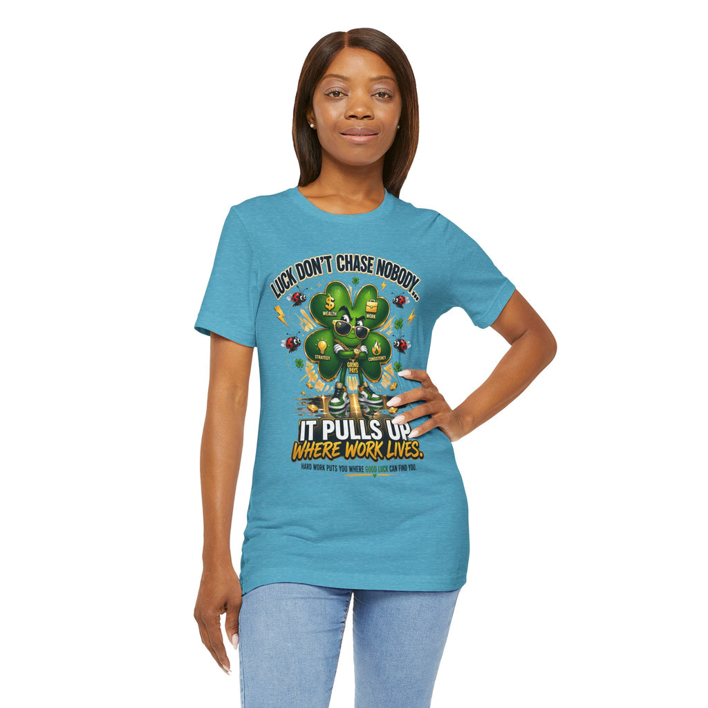 A woman smiles, wearing a TimeWarp Drip Lucky Clover "Pulls Up Lives" Graphic T-Shirt (sizes S–3XL, turquoise) featuring a cartoon clover and the text "Luck Don’t Chase Nobody, It Pulls Up Where Work Lives." Her left hand rests on her hip.