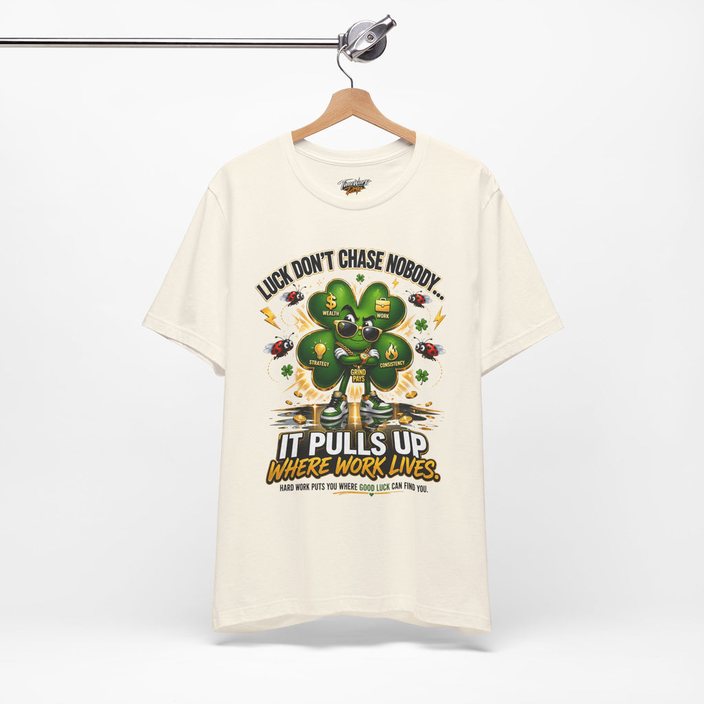 The TimeWarp Drip Lucky Clover "Pulls Up Lives" Graphic T-Shirt in cream (sizes S–3XL) features a four-leaf clover with money symbols and gold coins, plus the reminder: Hard work puts you where good luck can find you.