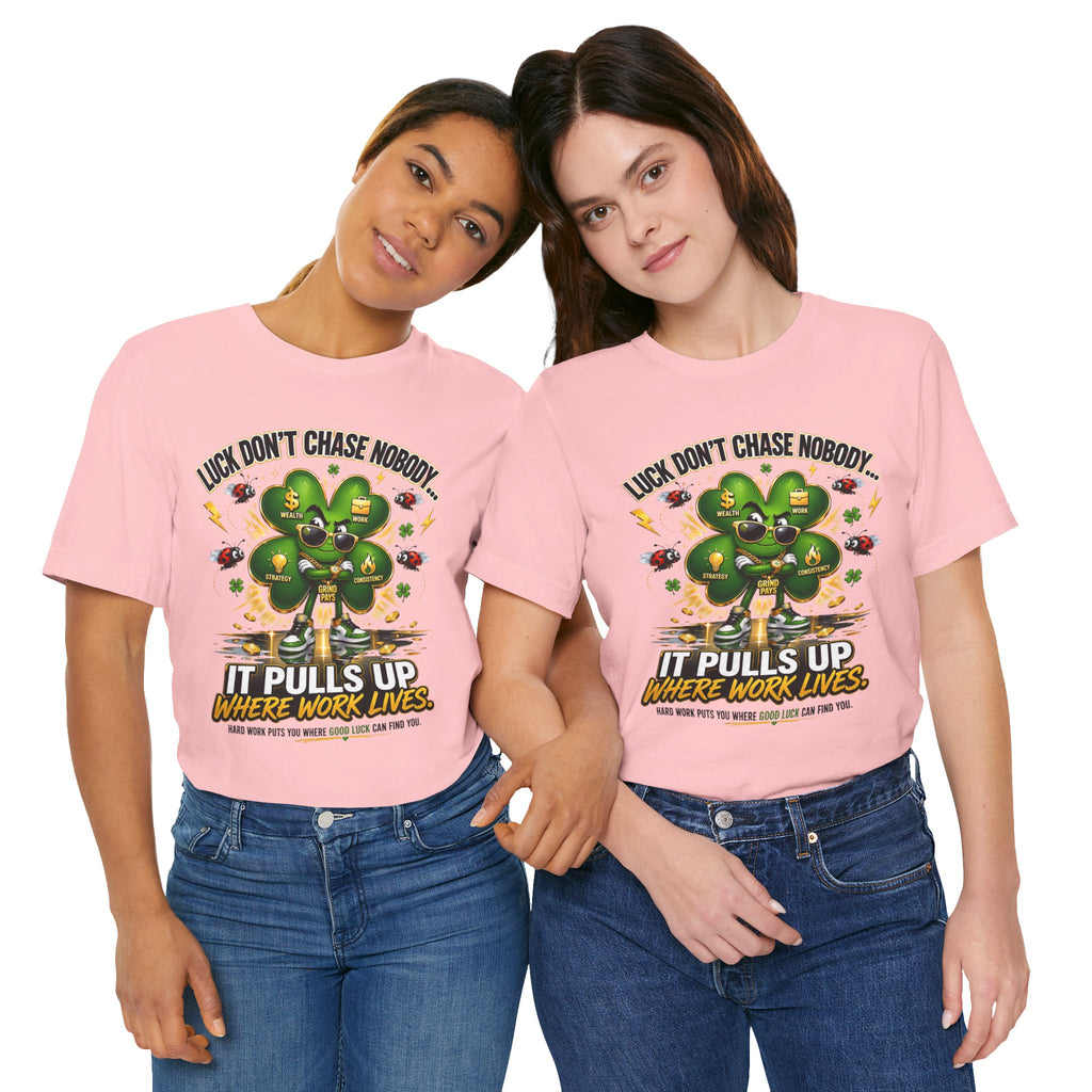 Two women smile together in matching TimeWarp Drip Lucky Clover “Pulls Up Lives” graphic t-shirts (S-3XL), featuring a four-leaf clover and the phrase: “Luck don’t chase nobody. It pulls up where work lives.”.