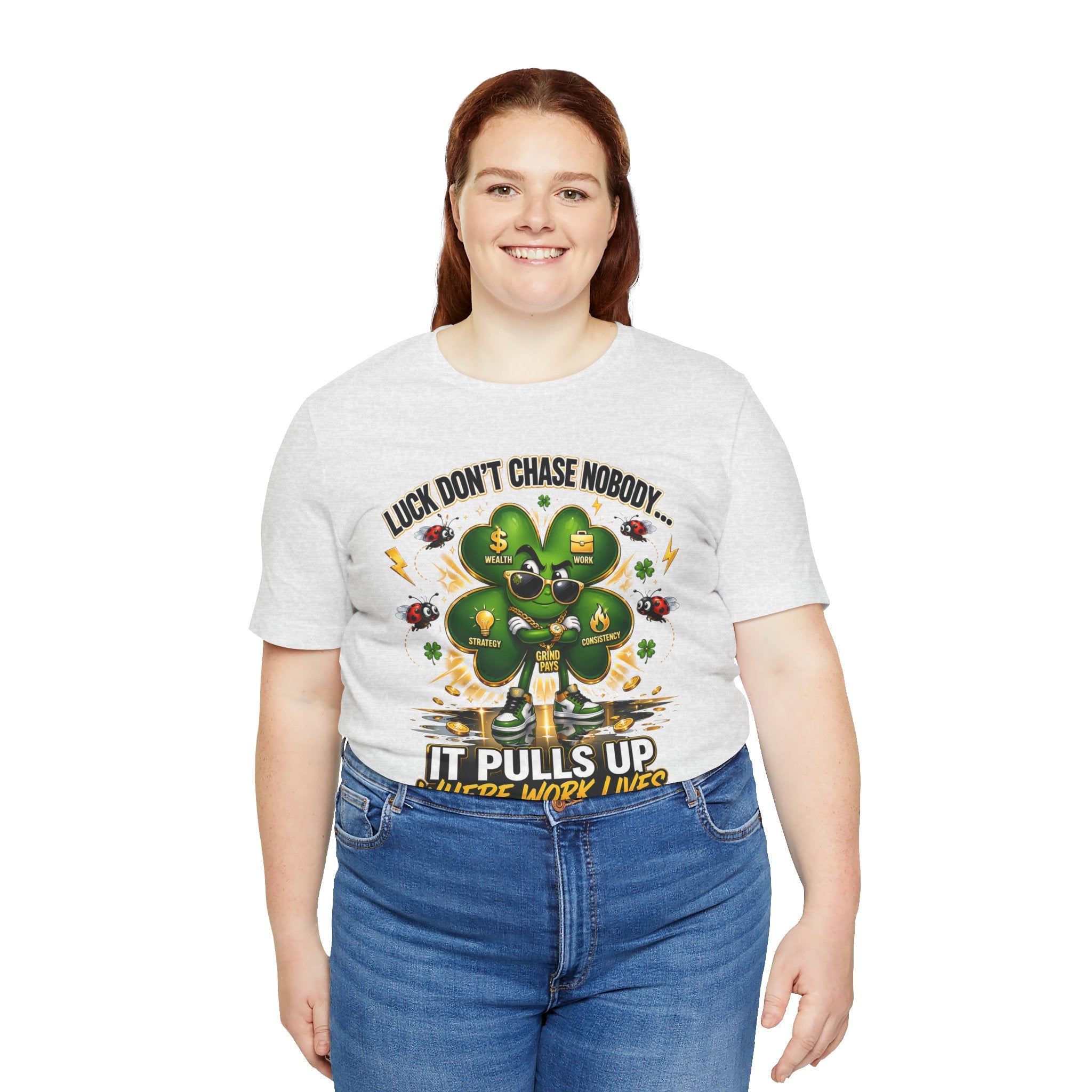 A smiling woman with long brown hair wears TimeWarp Drip's Lucky Clover "Pulls Up Lives" Graphic T-Shirt in light gray (sizes S-3XL), featuring a green four-leaf clover, bees, and the text: Luck, dont chase nobody. It pulls up where work lives.