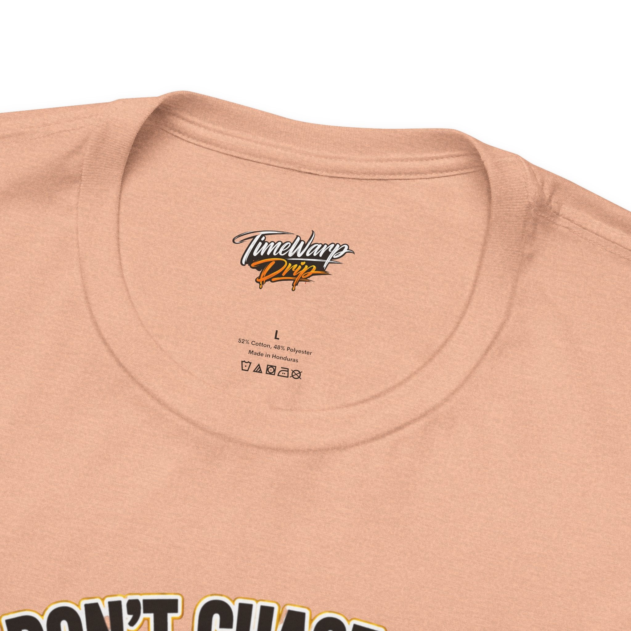 Close-up of a peach-colored Lucky Clover "Pulls Up Lives" Graphic T-Shirt by TimeWarp Drip, size L, with label and fabric info inside the collar. Available in S-3XL. Part of a text design is visible at the bottom edge.
