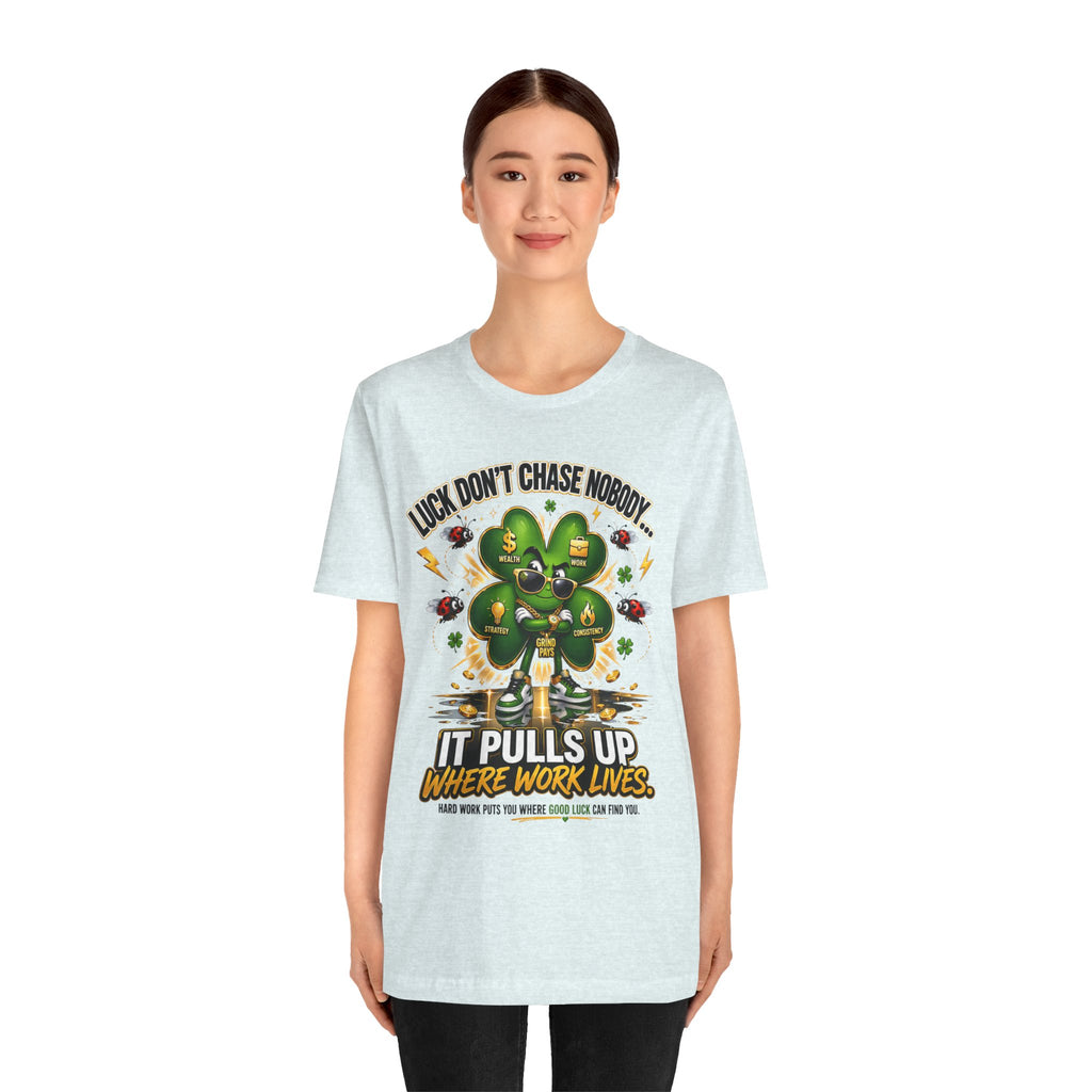 A young woman smiles in a TimeWarp Drip Lucky Clover "Pulls Up Lives" Graphic T-Shirt with a cartoon clover among coins. Sizes S-3XL. Shirt says: Luck don’t chase nobody. It pulls up where work lives.