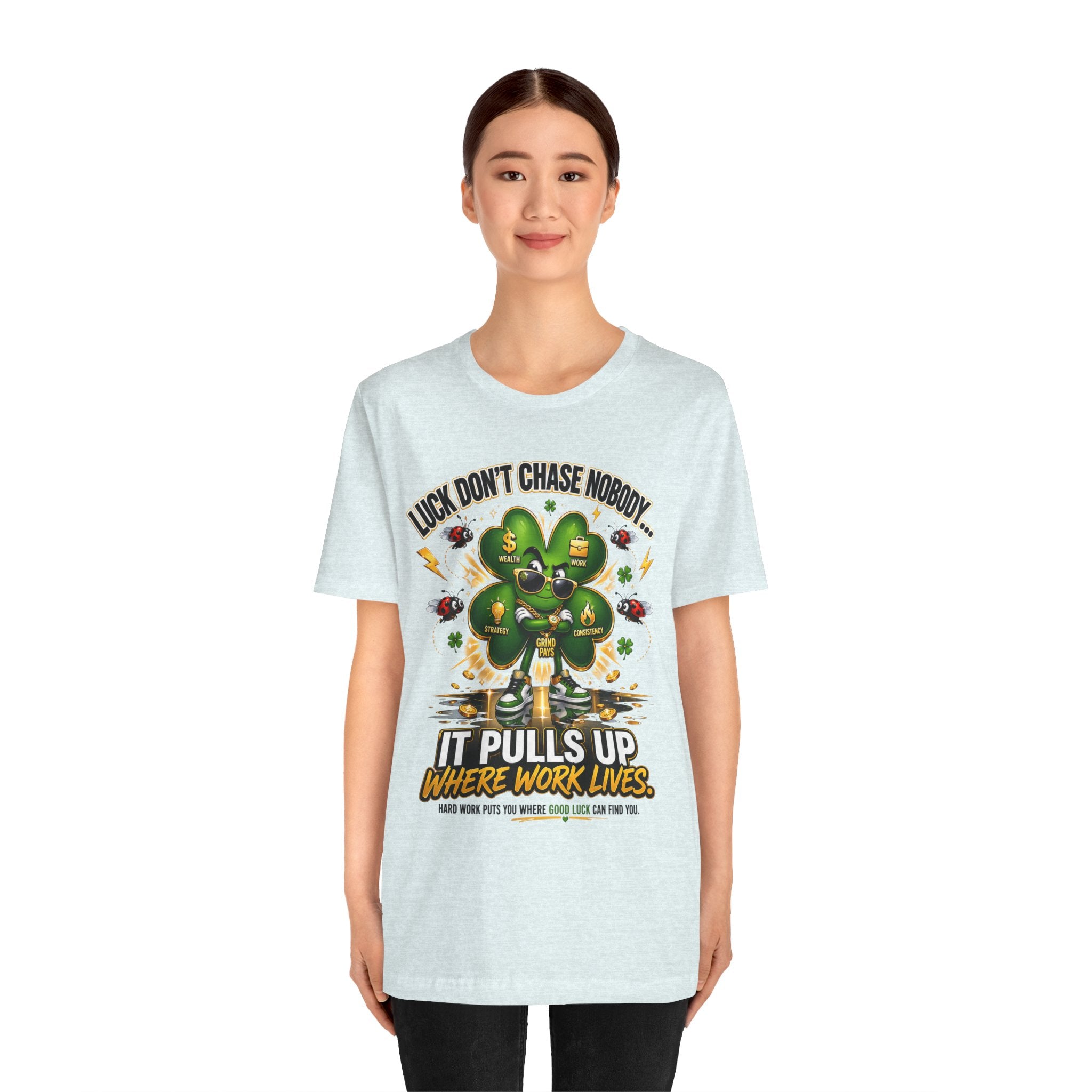 A young woman smiles in a TimeWarp Drip Lucky Clover "Pulls Up Lives" Graphic T-Shirt with a cartoon clover among coins. Sizes S-3XL. Shirt says: Luck don’t chase nobody. It pulls up where work lives.