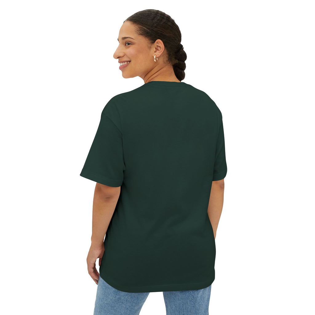 A woman with braided hair smiles over her shoulder, standing against a white background in light blue jeans and the Crowned In Every Era Unisex Oversized Boxy Tee.