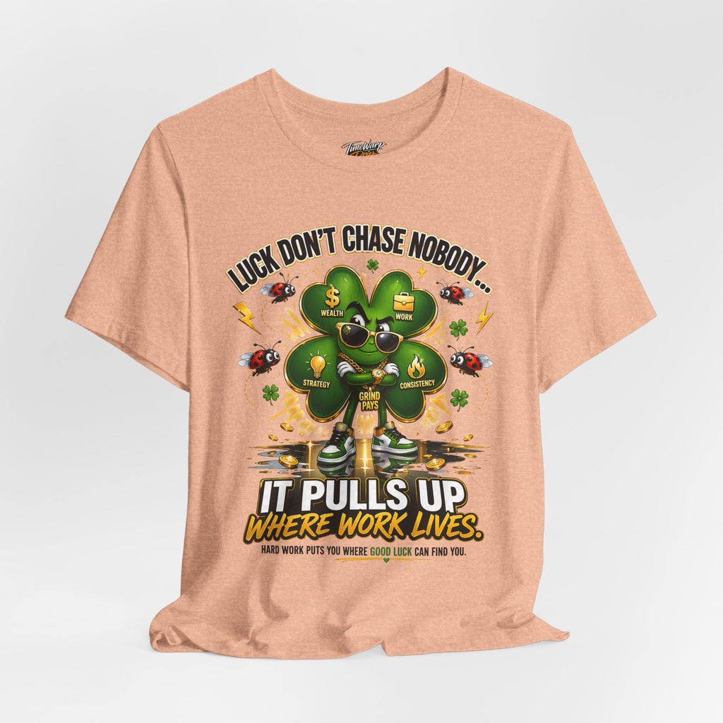 The TimeWarp Drip Lucky Clover "Pulls Up Lives" Graphic T-shirt, in peach (S-3XL), features a clover with sunglasses and gold chains, ladybugs, dollar signs, confetti, and the text: “Luck Don’t Chase Nobody… It Pulls Up Where Work Lives.”.