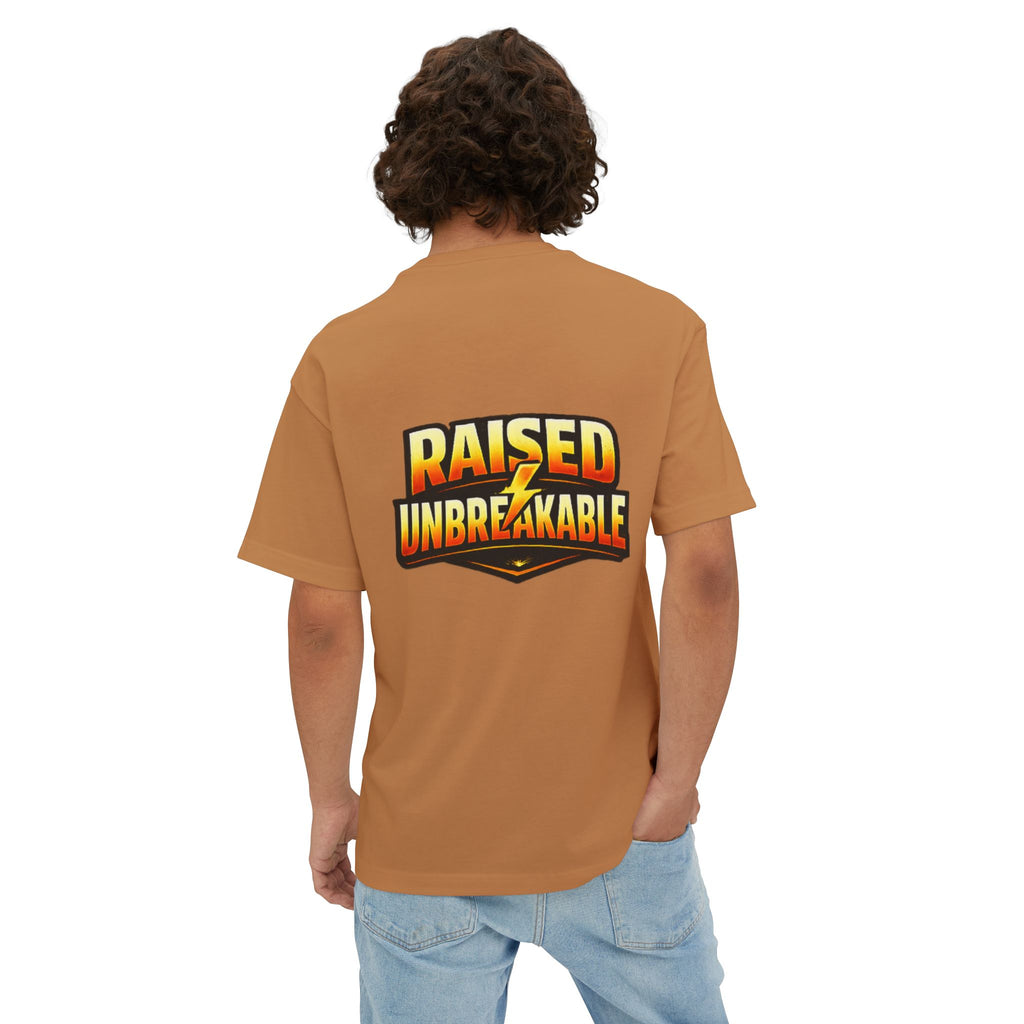 A person with curly hair, seen from behind, wears the oversized boxy "Come Get Em" tee by TimeWarp Drip. The breathable brown T-shirt features bold yellow and red RAISED UNBREAKABLE text on the back. One hand is casually tucked in their pocket.