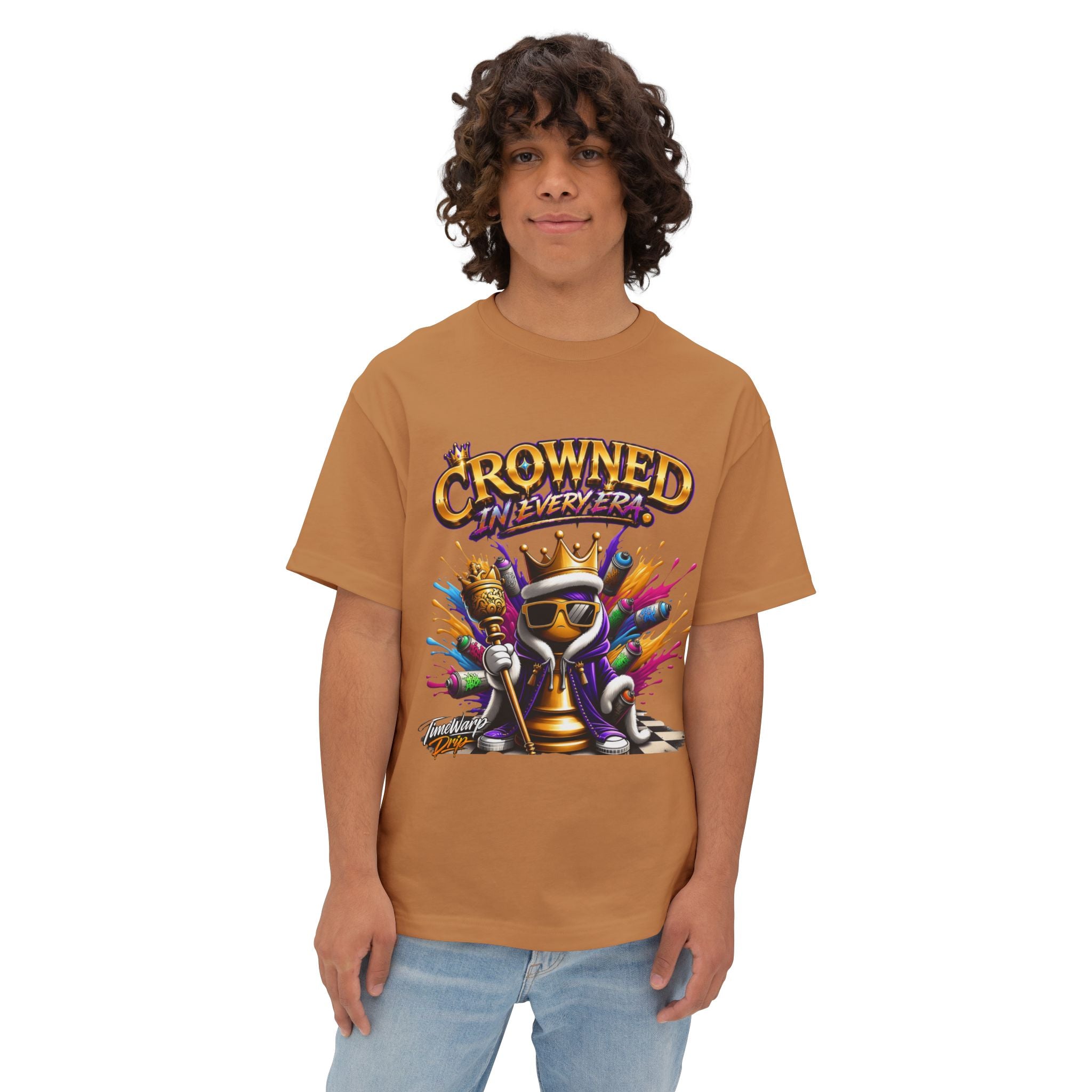 A young person with curly hair wears the Crowned In Every Era - Unisex Oversized Boxy Tee, a relaxed fit brown shirt with a colorful cartoon king chess piece graphic and bold text, standing confidently against a plain white background.