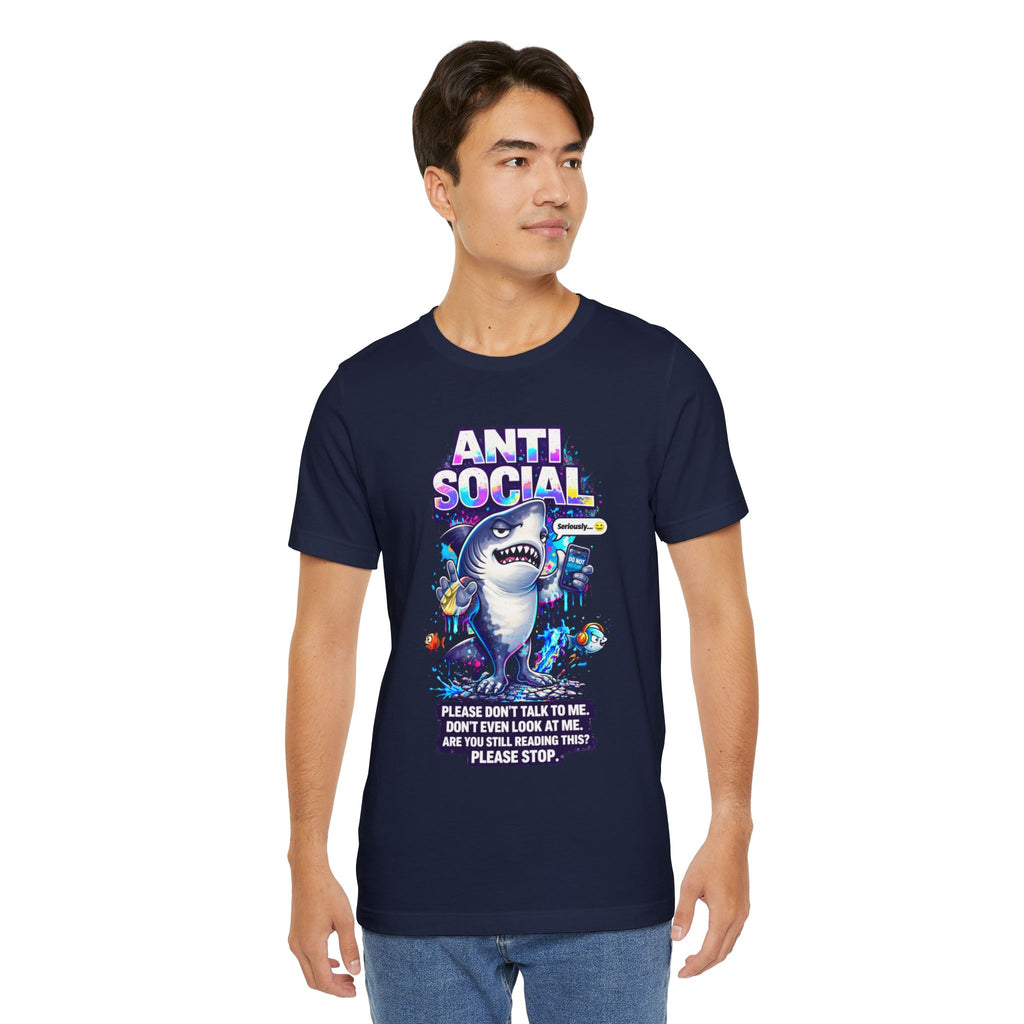 A man wears the Anti Social Shark T-Shirt — Funny Introvert Graphic Tee, a navy blue unisex cotton shirt with a cartoon shark and text: ANTI SOCIAL and "Please don’t talk to me, don’t even look at me. Are you still reading this? Please stop.