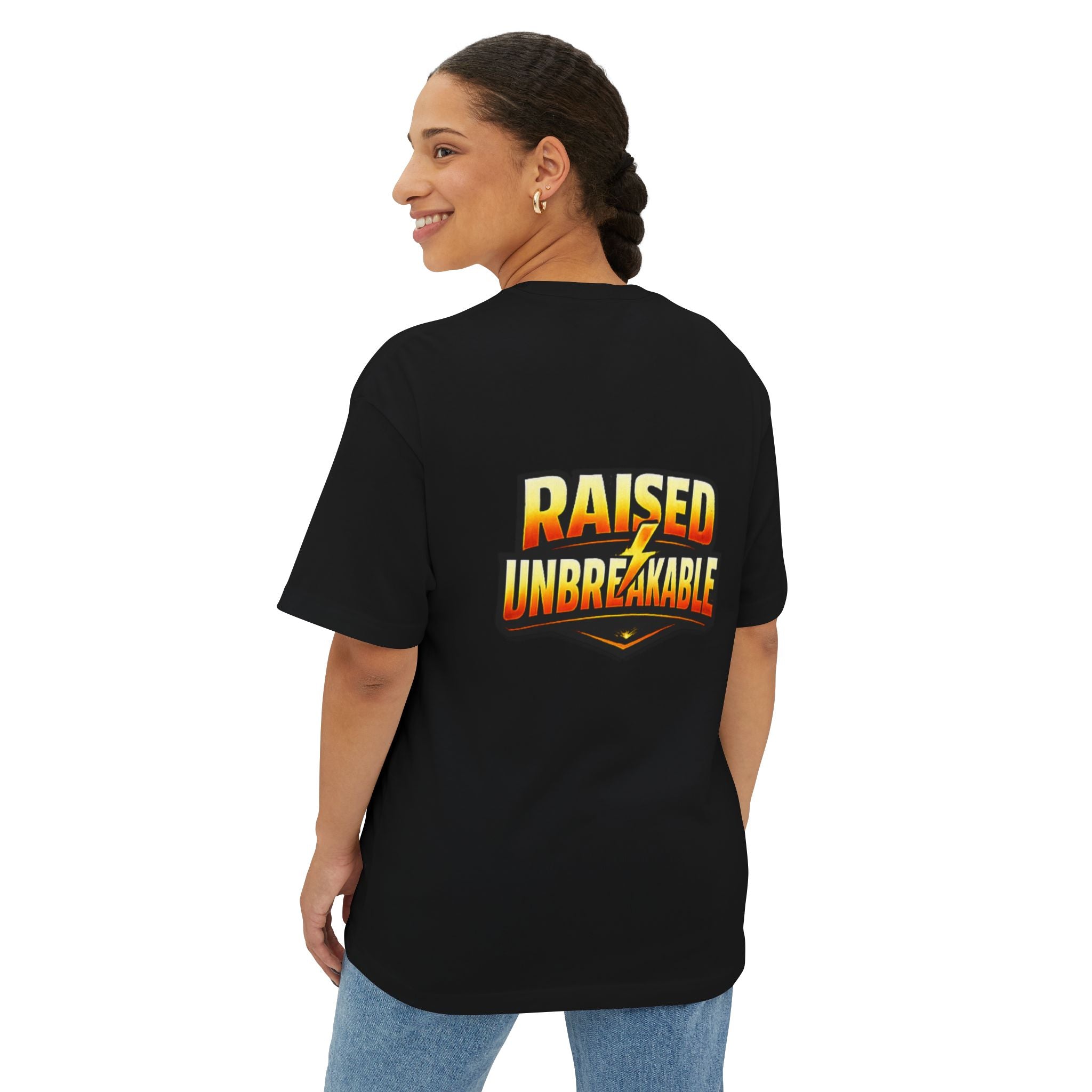 A woman with braided hair smiles over her shoulder, wearing the TimeWarp Drip Generation X Parenting "Come Get Em" oversized boxy tee. The black cotton T-shirt features a yellow and orange “RAISED UNBREAKABLE” text graphic on the back.