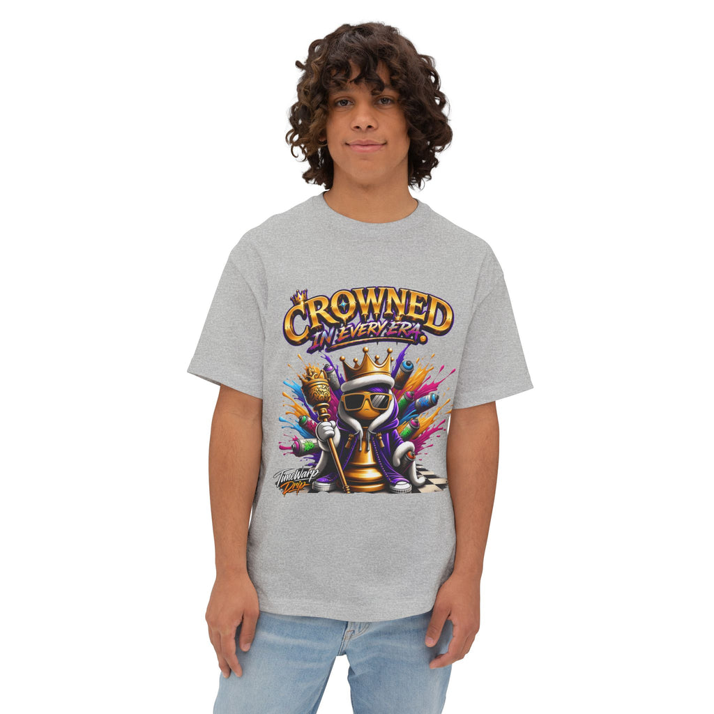 A young person with curly hair wears the Crowned In Every Era - Unisex Oversized Boxy Tee, a relaxed fit light gray shirt made with airlume combed cotton, featuring a cartoon king chess piece and "CROWNED IN EVERY ERA" above the design.