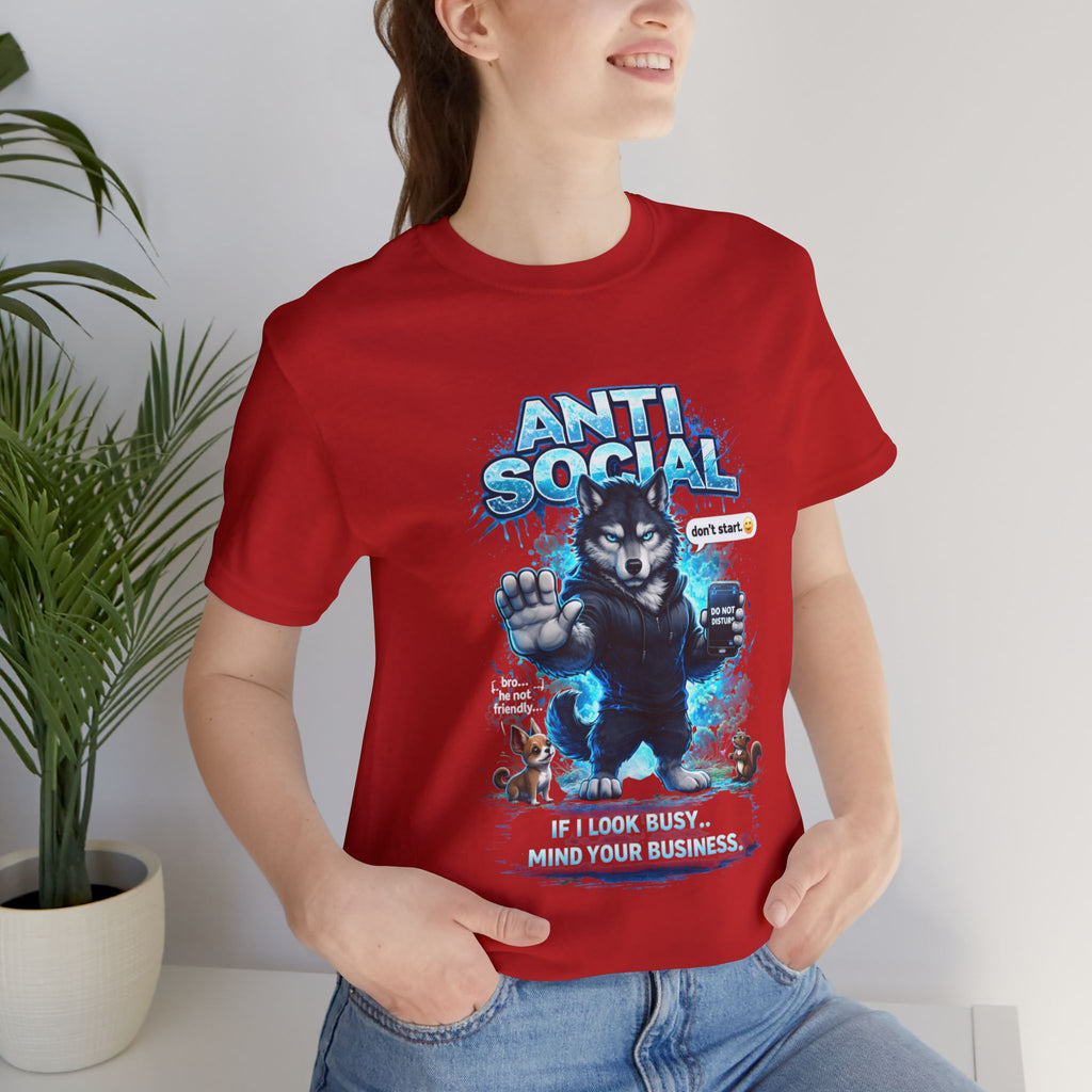 A woman smiles by plants in a red Timewarp Drip Anti Social Wolf T-Shirt—Funny Introvert Graphic Tee featuring a grumpy cartoon wolf with paw raised, blue graphics, small animals, and the phrase “ANTI SOCIAL—If I look busy, mind your business.”.