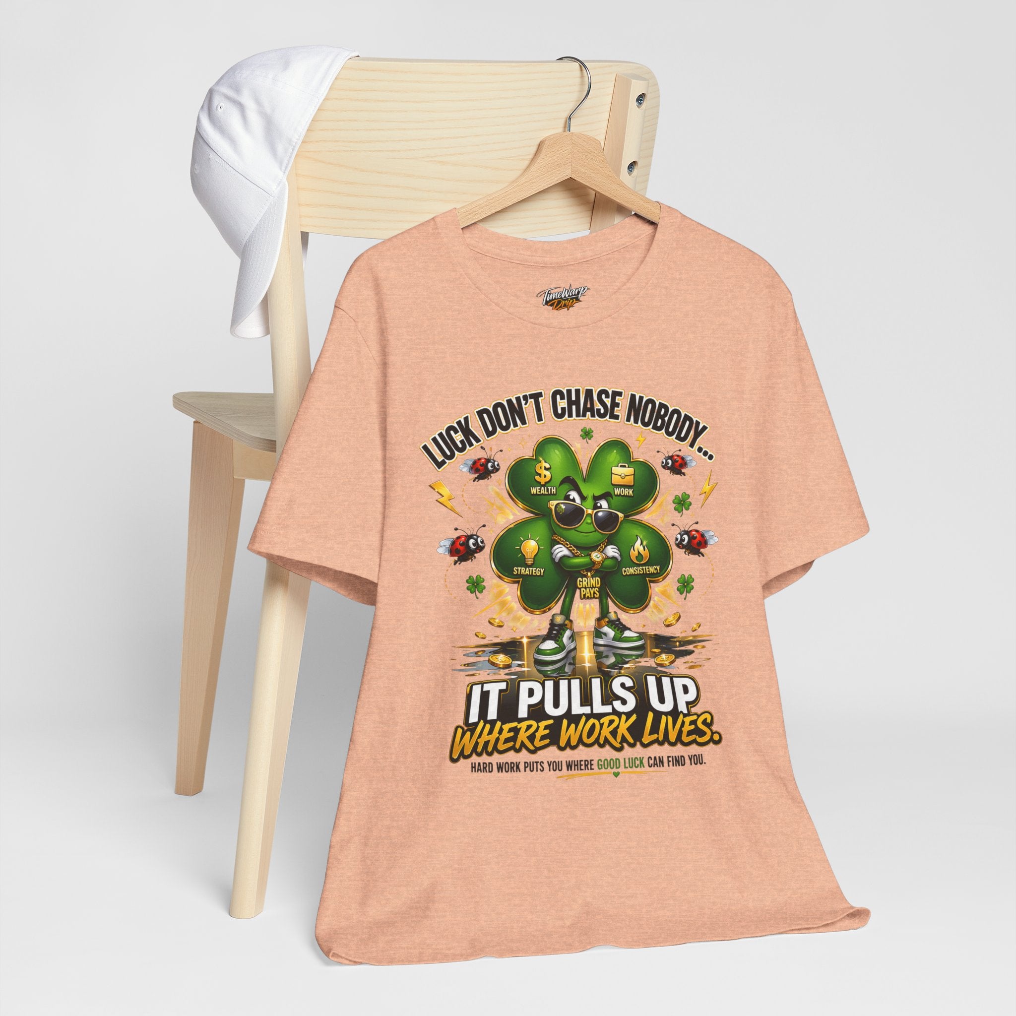 TimeWarp Drip Peach "Luck Don’t Chase Nobody" tee with bold 4-leaf clover drip, street-cool on a chair beside a crisp white cap. streetwear apparel