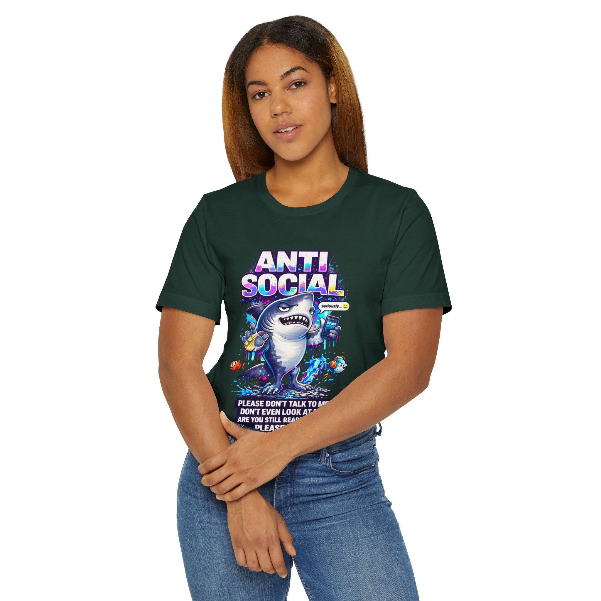 A woman with straight, long brown hair wears a dark green Anti Social Shark T-Shirt — Funny Introvert Graphic Tee, featuring a playful shark graphic and vibrant colors, standing with hands loosely clasped and looking at the camera.